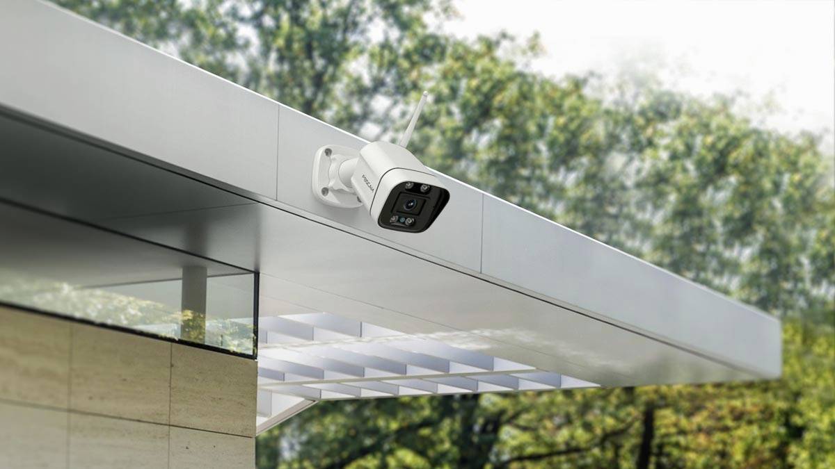 Caméra de surveillance sur le mur extérieur d'un bâtiment moderne avec des arbres en arrière-plan, symbolisant la sécurité et la surveillance.