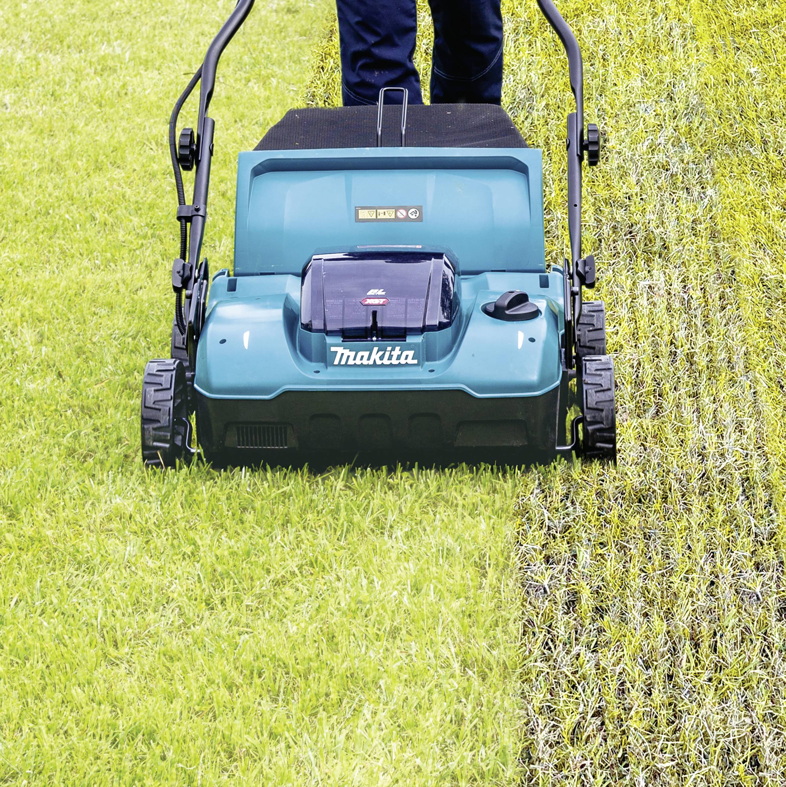 Une personne tond l'herbe avec une tondeuse bleue. À gauche, l'herbe est haute, à droite se trouve une bande déjà tondue.