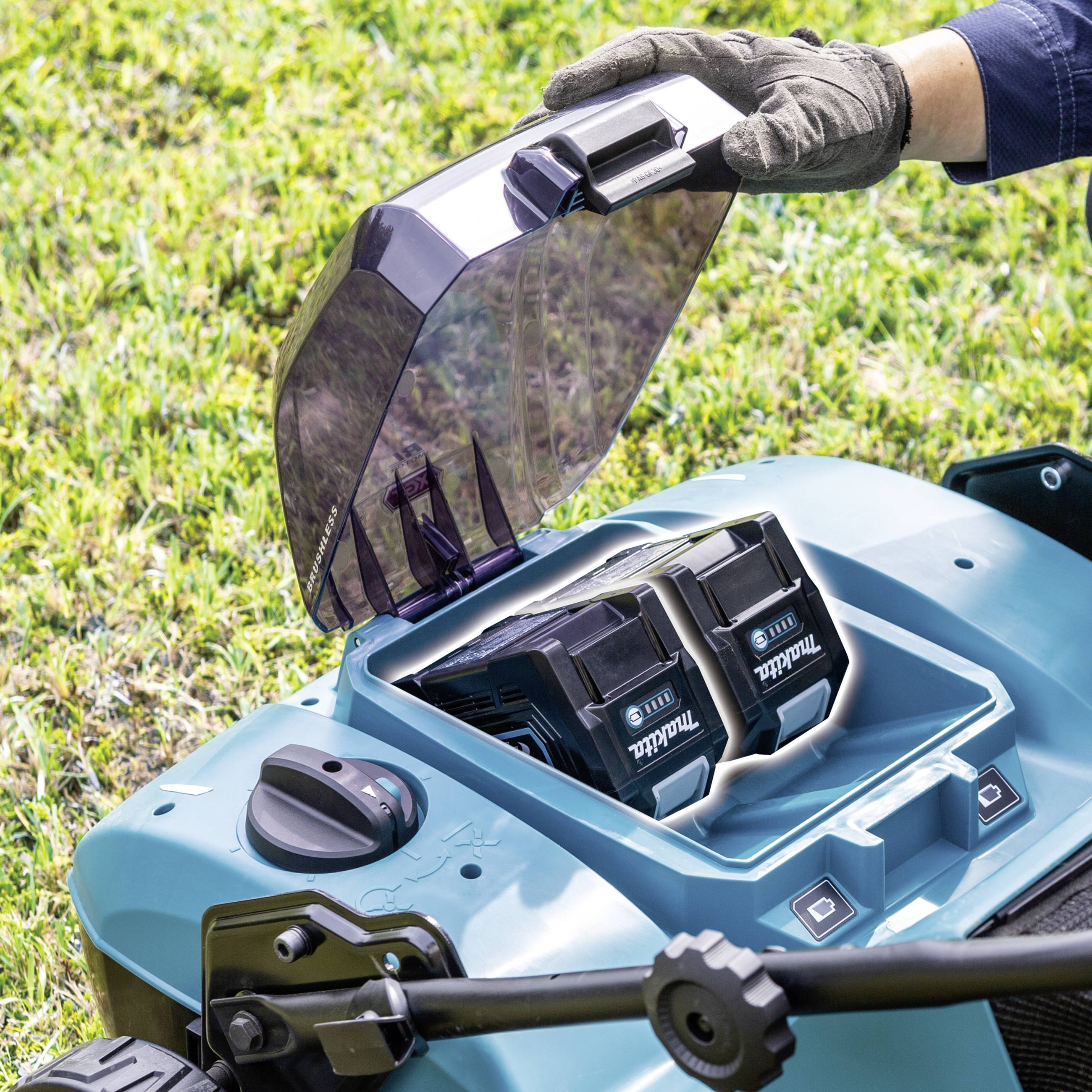 Ouvre un robot tondeuse, montrant deux batteries à l'intérieur. Porte un gant de jardinage, démontrant l'entretien ou le remplacement des batteries de l'appareil.