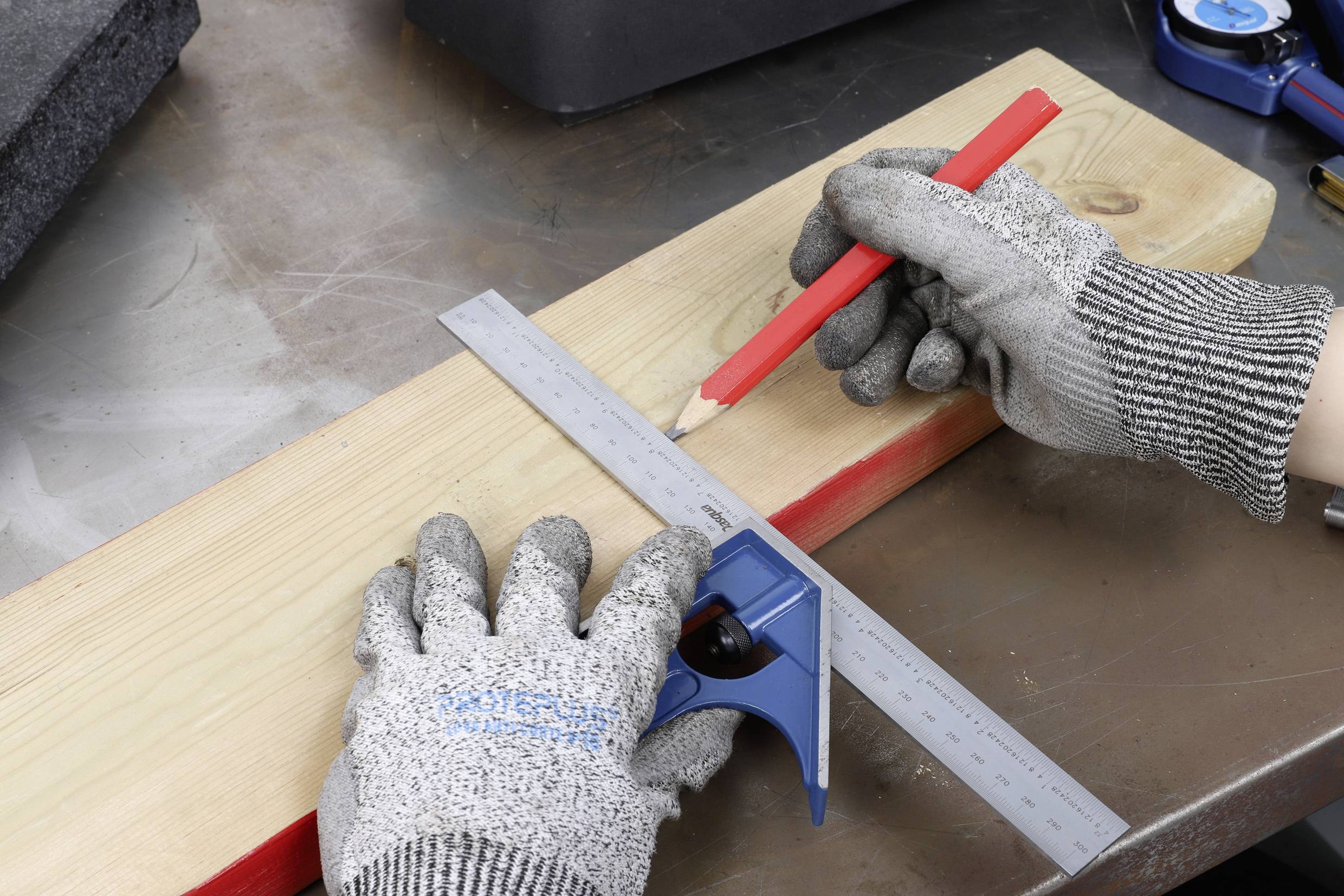 Une personne portant des gants gris mesure avec un rapporteur et un crayon rouge sur une planche en bois.