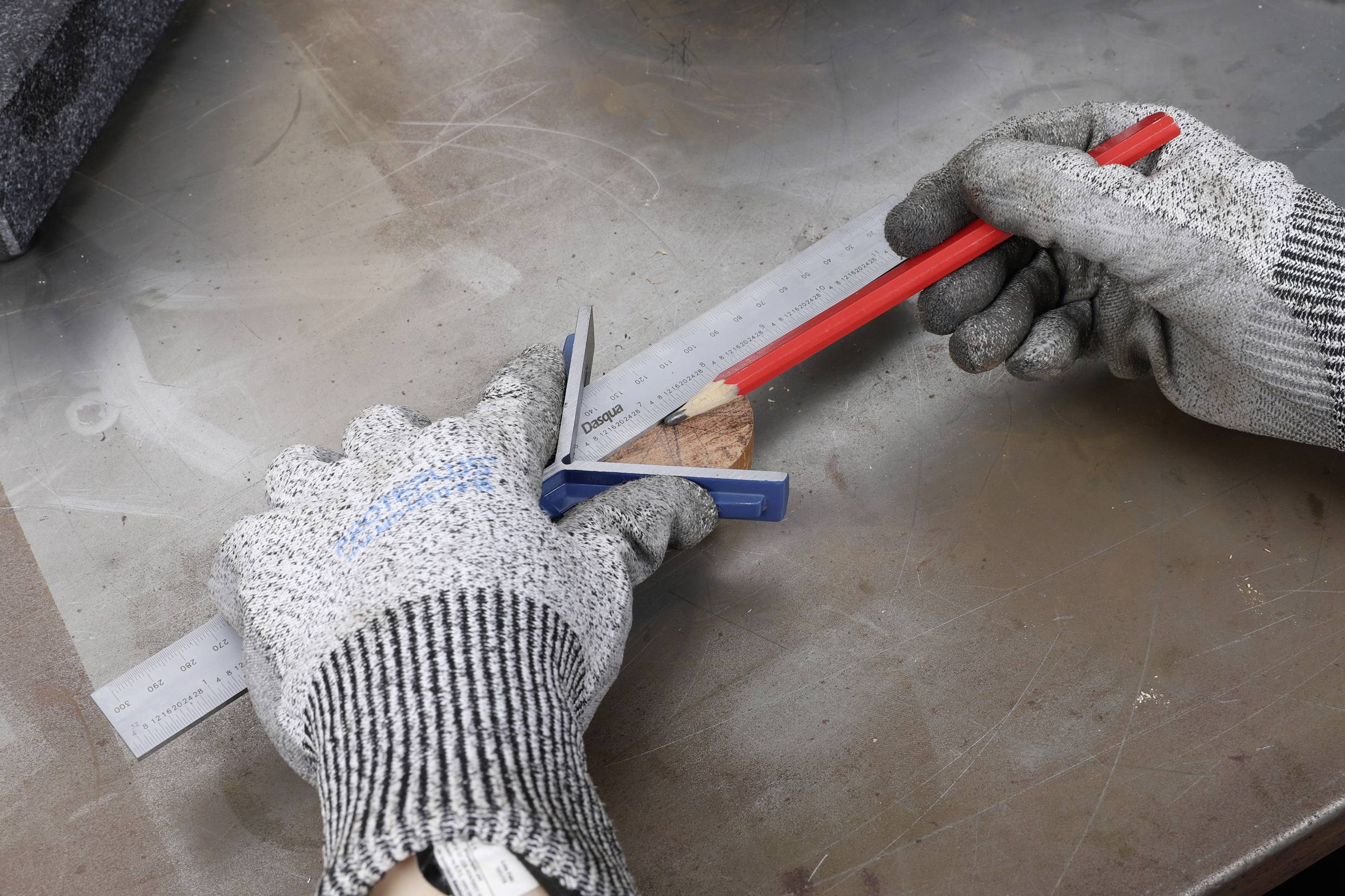 Un couple de mains gantées mesure et marque avec une règle et un crayon sur un morceau de bois.