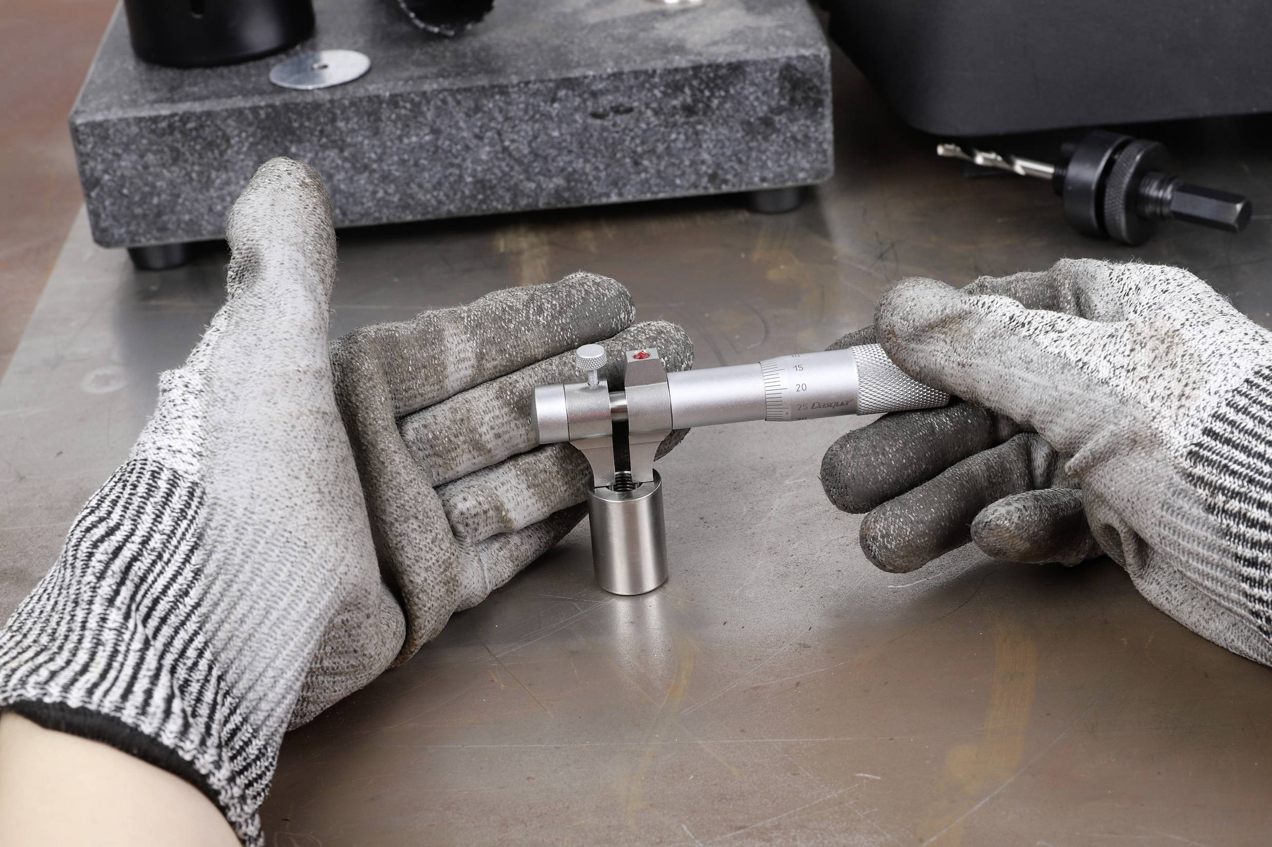 Une personne portant des gants de protection utilise un instrument de mesure de précision sur une surface métallique afin de mesurer l'épaisseur d'une pièce.