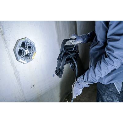 Une personne travaille avec un outil près d'un boîtier de raccordement rond monté sur le mur. Elle porte des vêtements robustes et des gants.