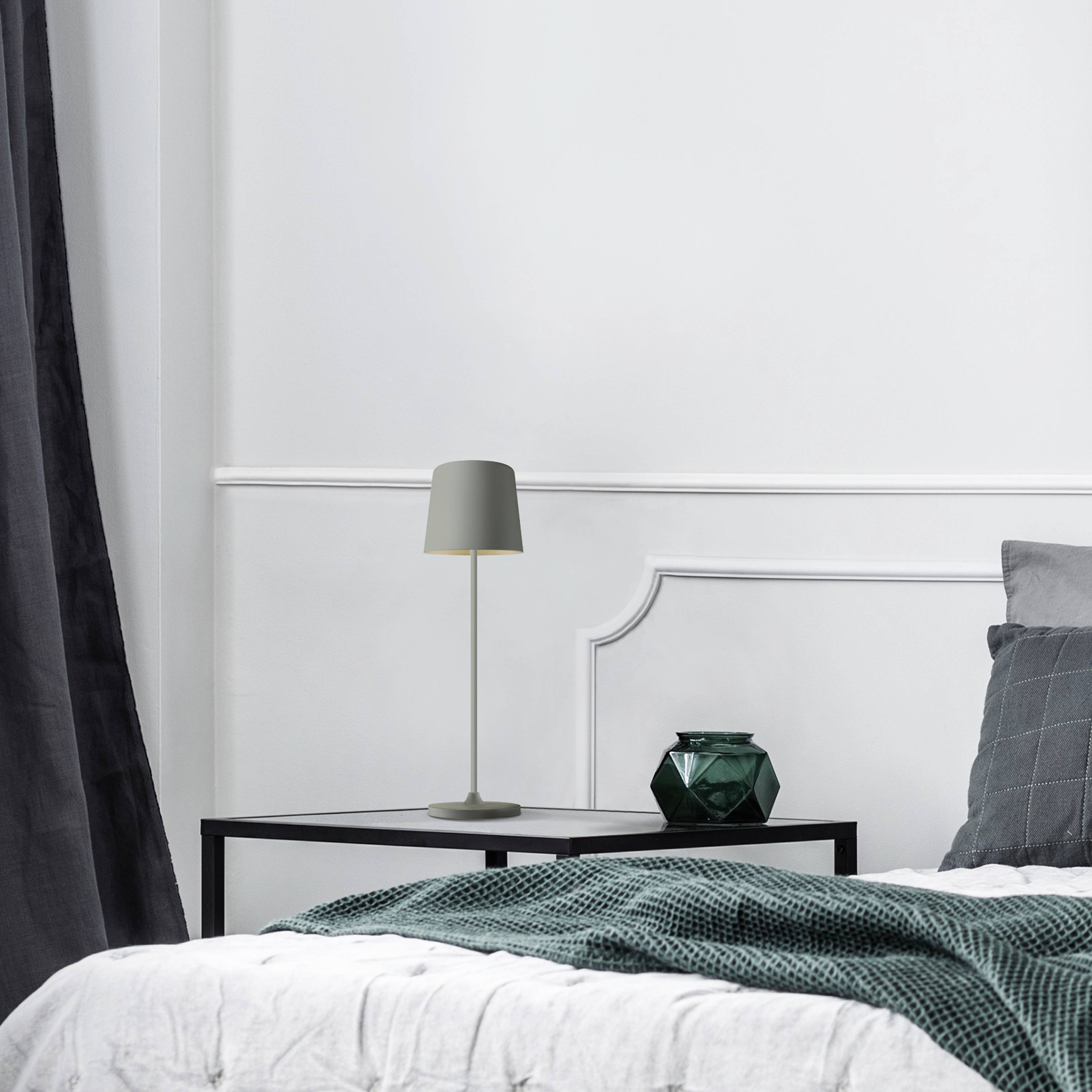 Une chambre moderne avec une couette blanche, une couverture et des coussins verts. Une lampe est posée sur la table de chevet à côté.
