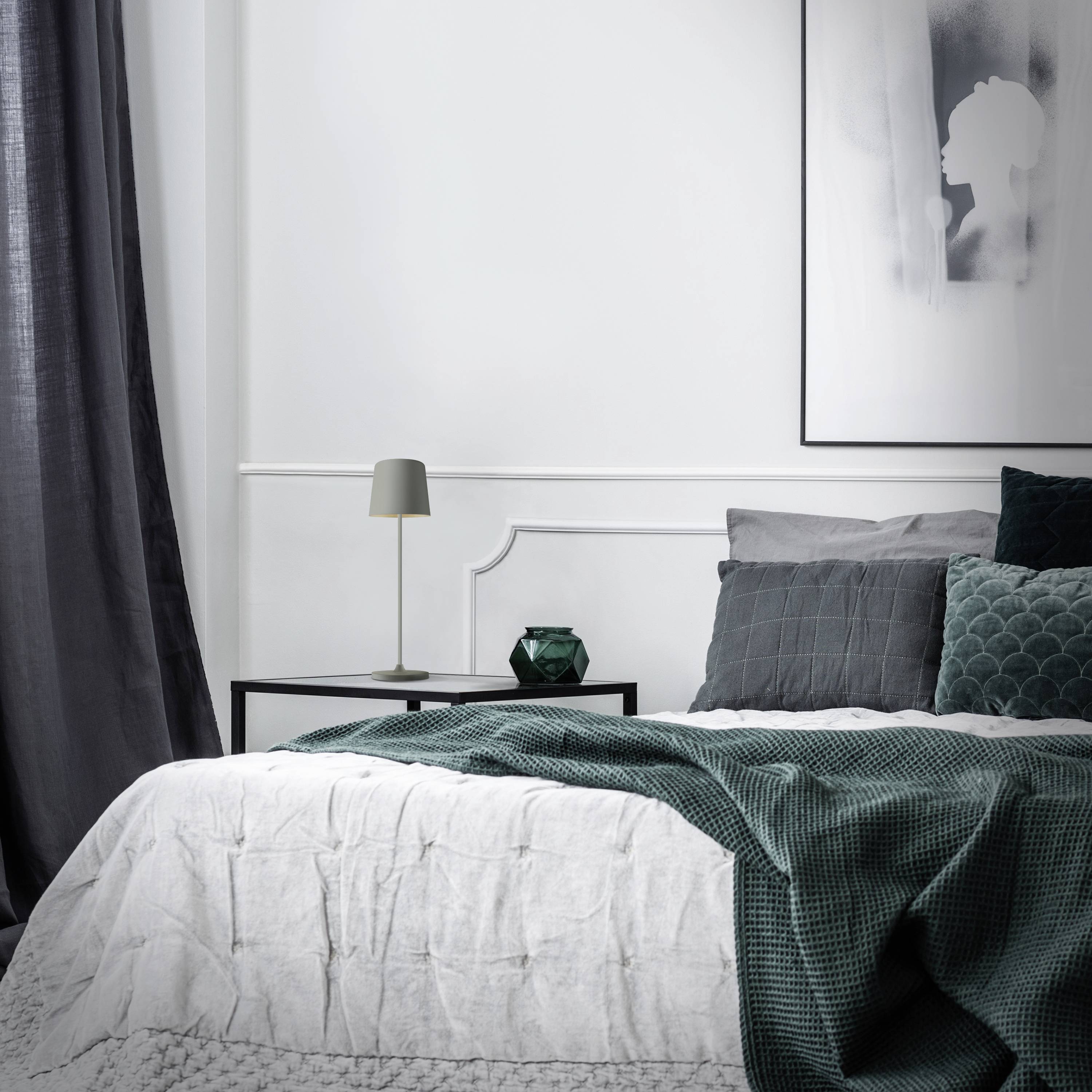 Une chambre élégante avec un rideau gris, un lit blanc avec des coussins verts et une petite lampe de chevet sur une table de nuit.