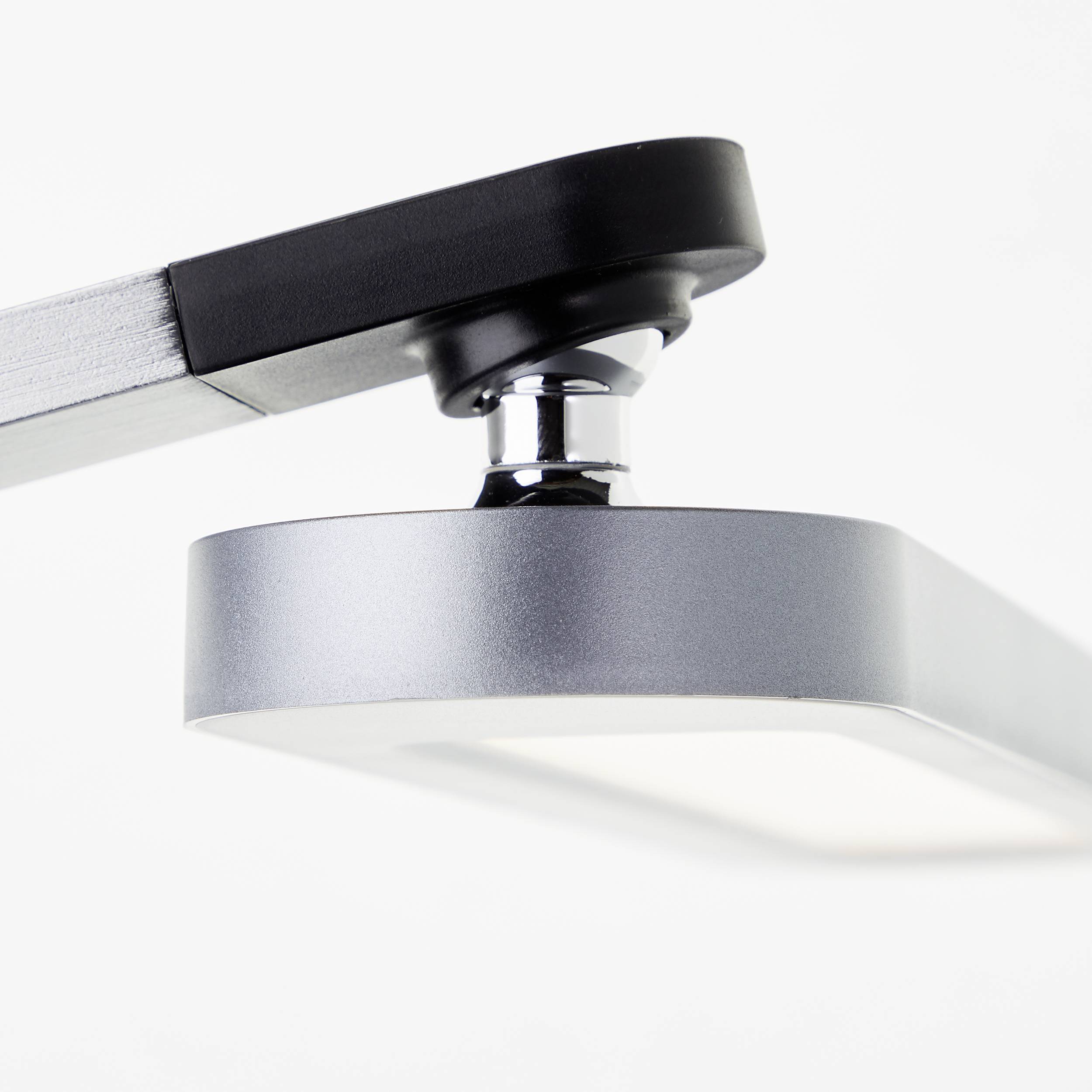 Une lampe de bureau moderne en argent avec un corps lumineux rectangulaire et un bras articulé noir, vue en gros plan.