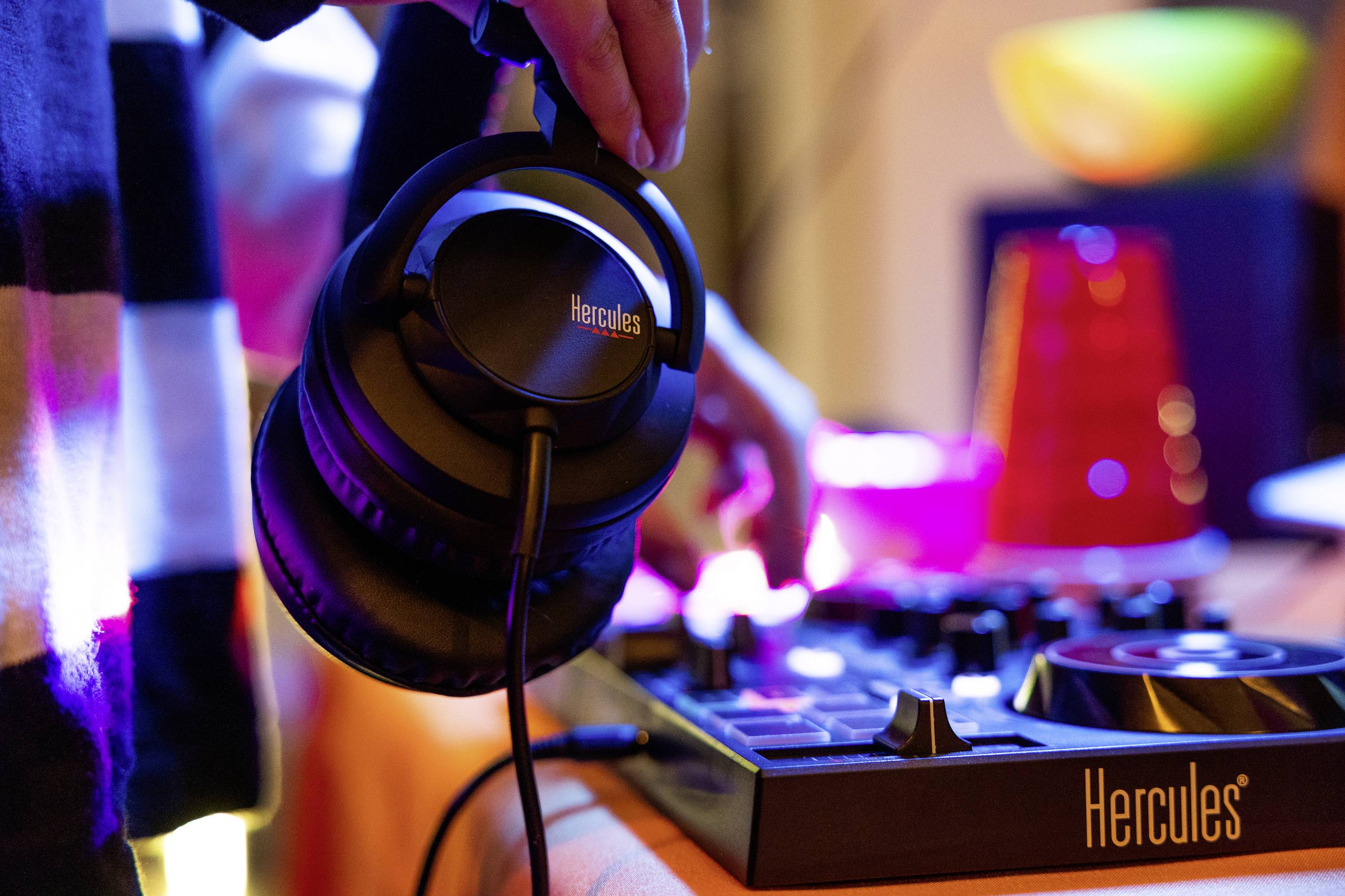 Une personne tient des écouteurs au-dessus d'un contrôleur DJ. Des lumières colorées et des objets sont visibles en arrière-plan.