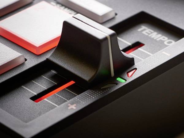 Gros plan sur une table de mixage noire avec un curseur de réglage du tempo, des touches rétroéclairées et un indicateur LED rouge.
