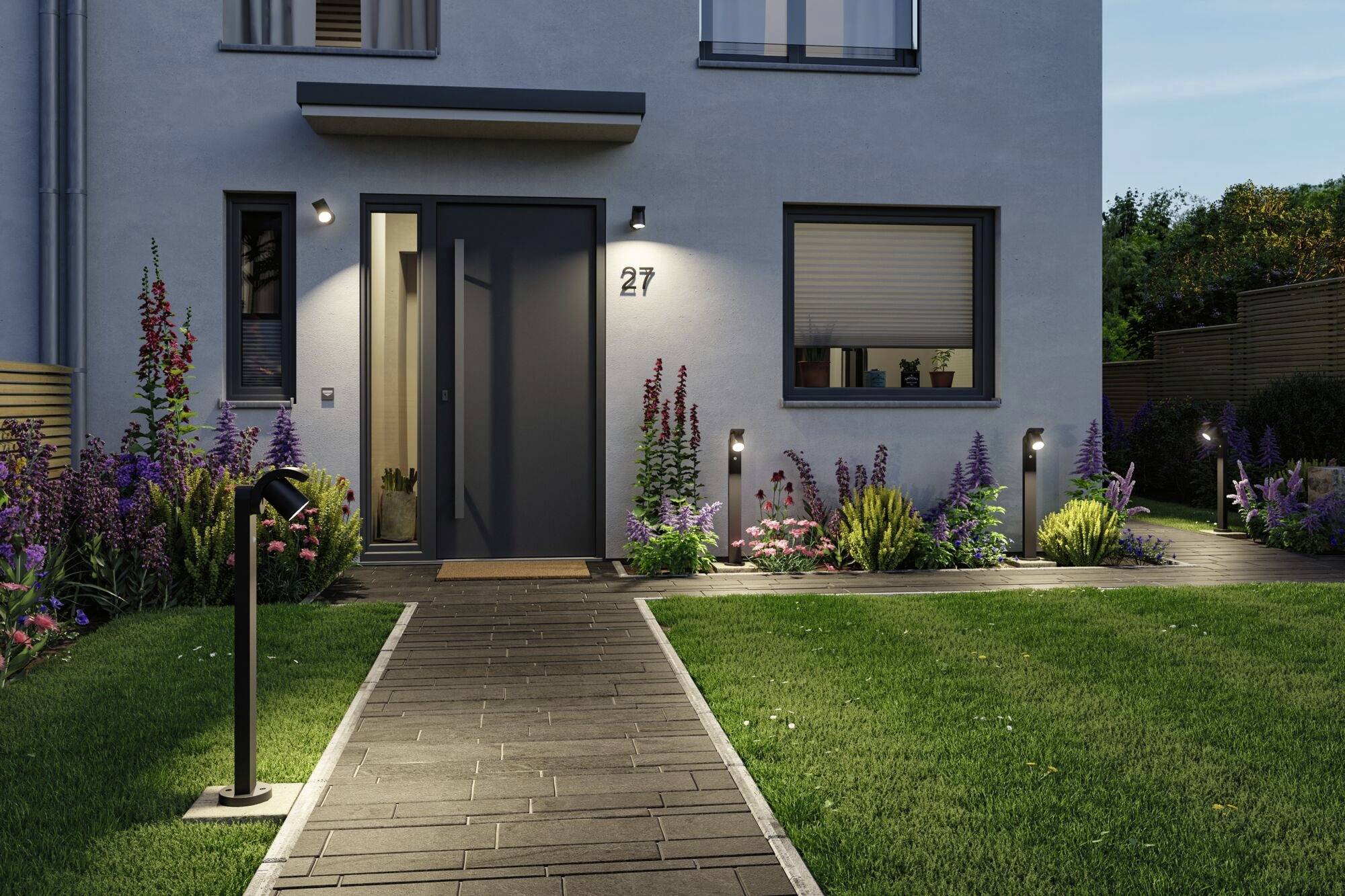 Façade de maison moderne avec un espace d'entrée éclairé, entourée d'un jardin soigné aux fleurs colorées et aux pelouses uniformes.