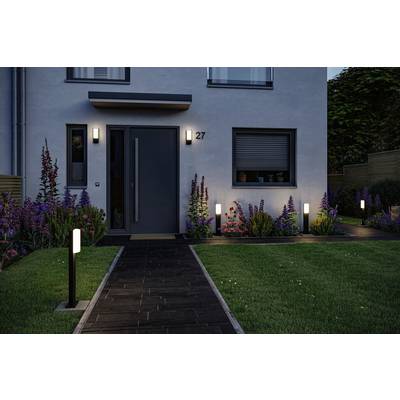 Une maison moderne au crépuscule avec une entrée illuminée et un éclairage de jardin. Des parterres de fleurs bordent le chemin pavé.