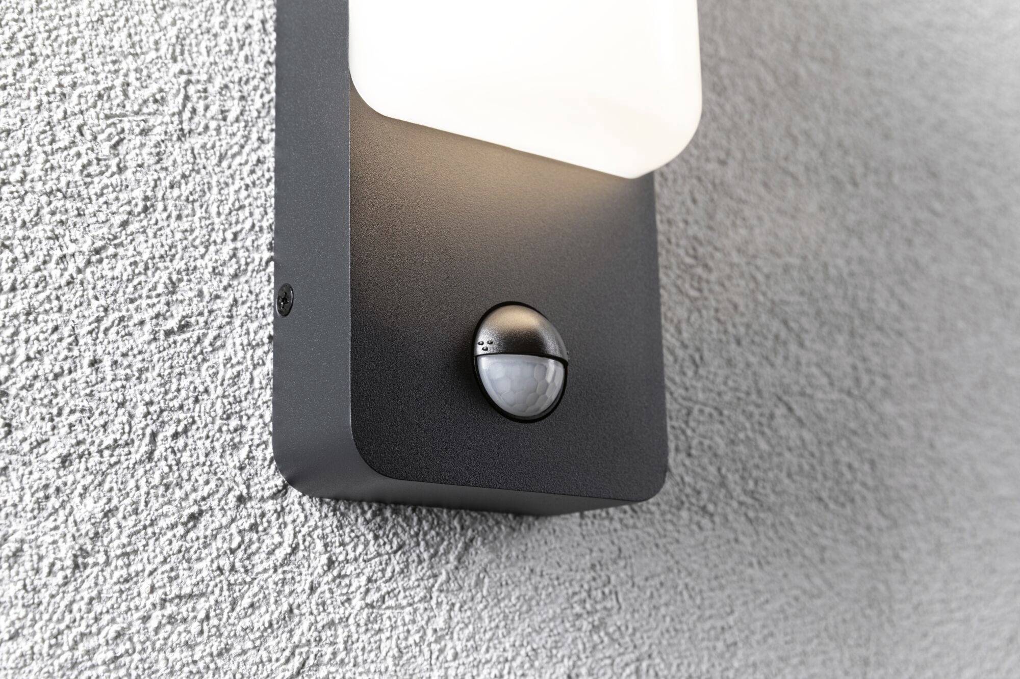 Lampe extérieure avec capteur de mouvement intégré sur un mur gris.