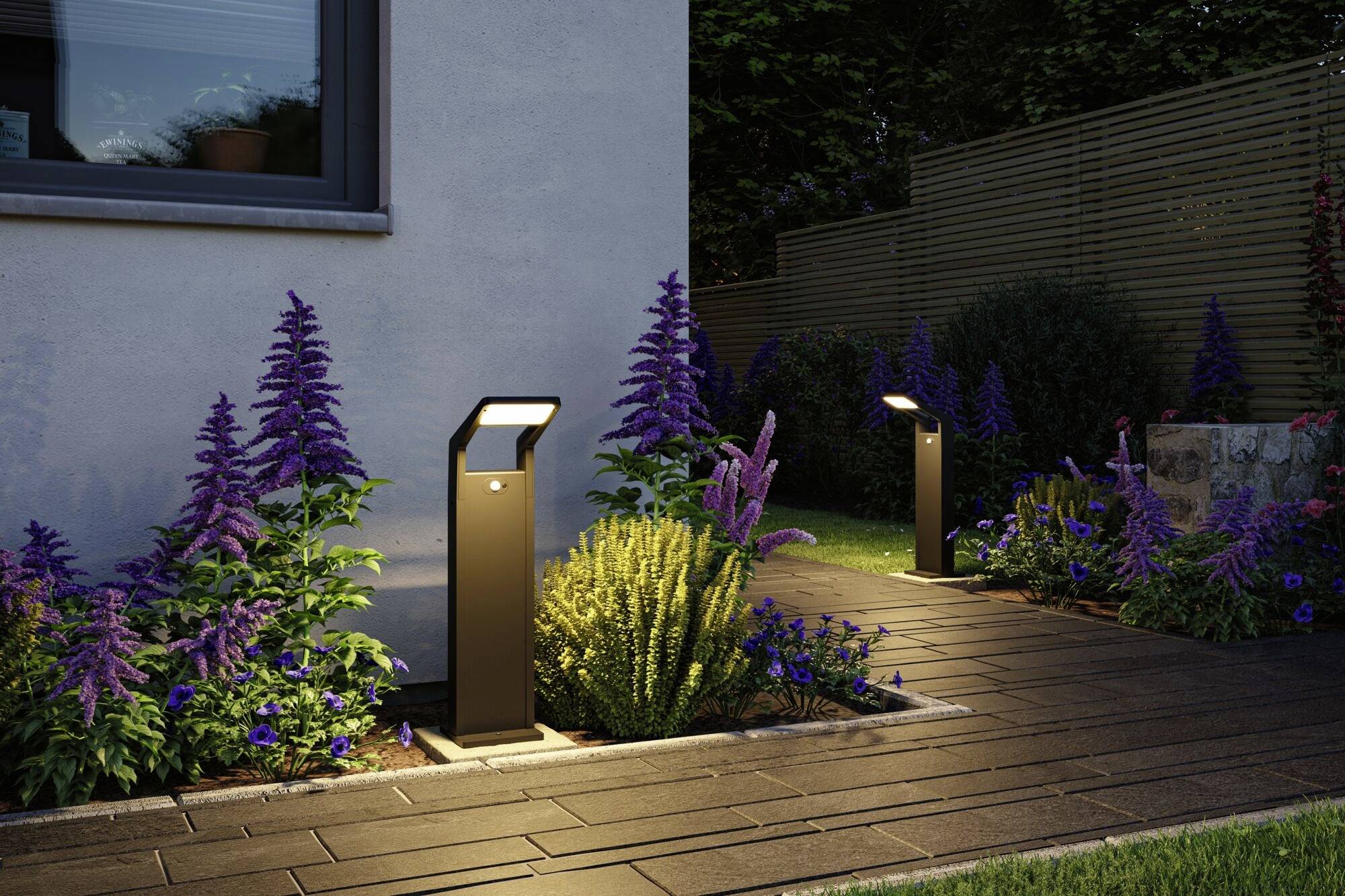 Allée de jardin bordée de luminaires modernes, flanquée de massifs de fleurs lilas luxuriants le long du mur de la maison, éclairée au crépuscule.