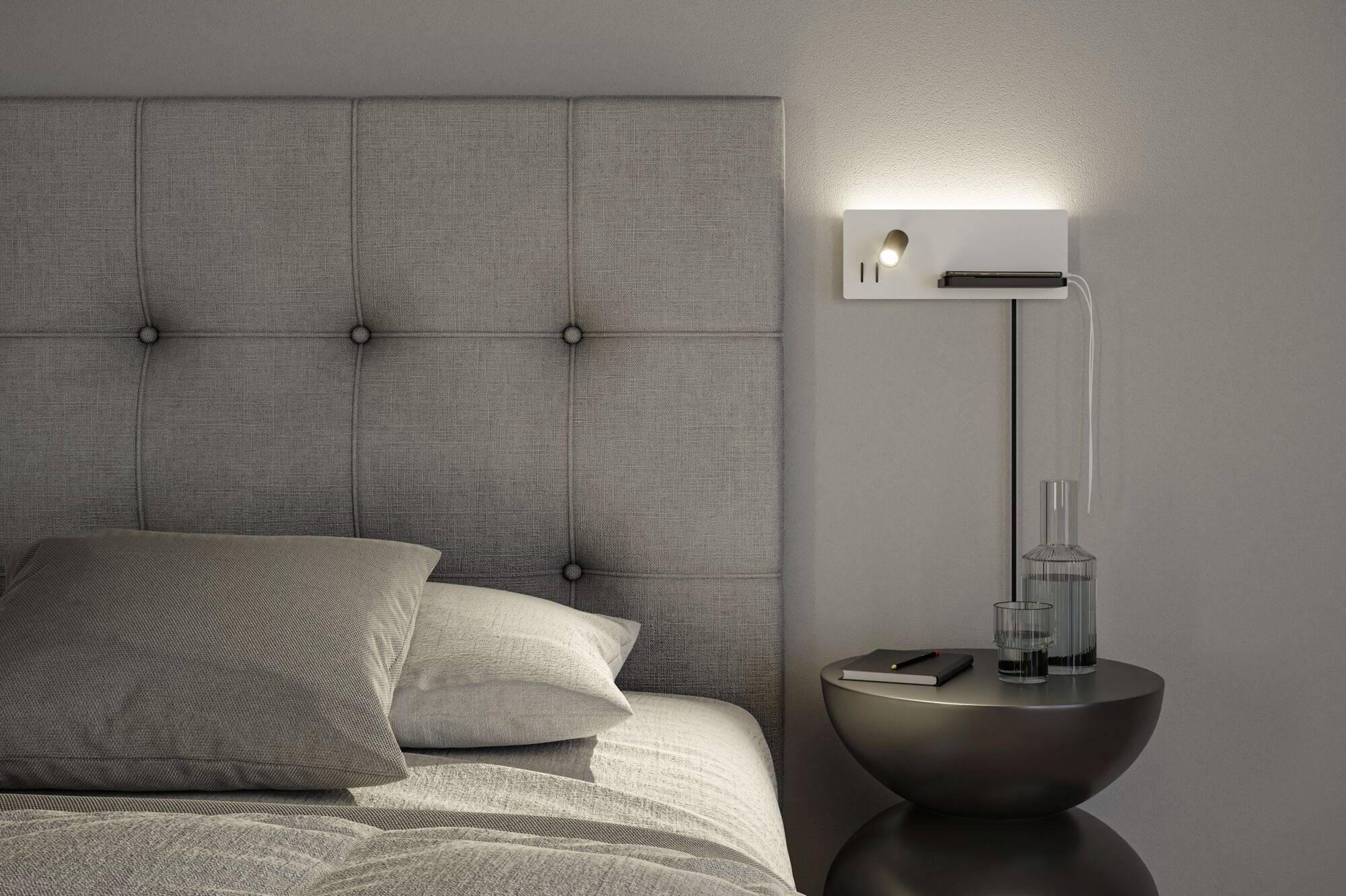 Une chambre moderne avec une tête de lit grise, une table de chevet avec un verre d'eau et un smartphone, éclairée par une applique murale.