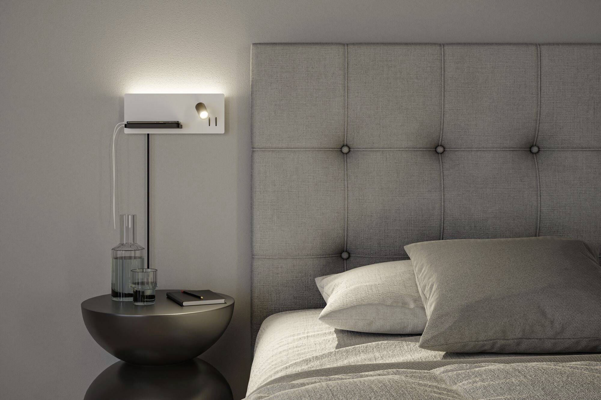 Une chambre confortable avec une tête de lit grise, un lit recouvert de draps gris et une table de chevet avec une lampe et un verre d'eau.