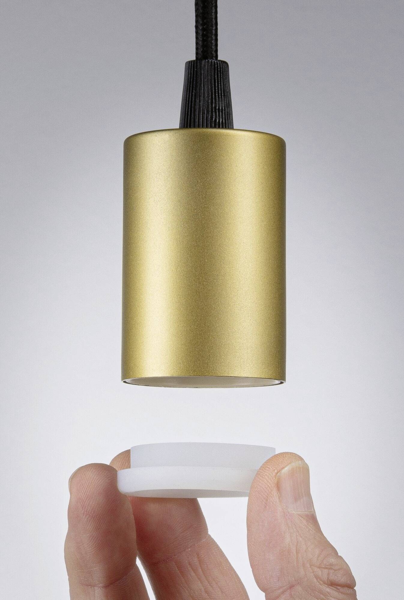 Une main tient un disque rond et blanc sous une suspension cylindrique dorée. L'image montre la manipulation de la lumière.