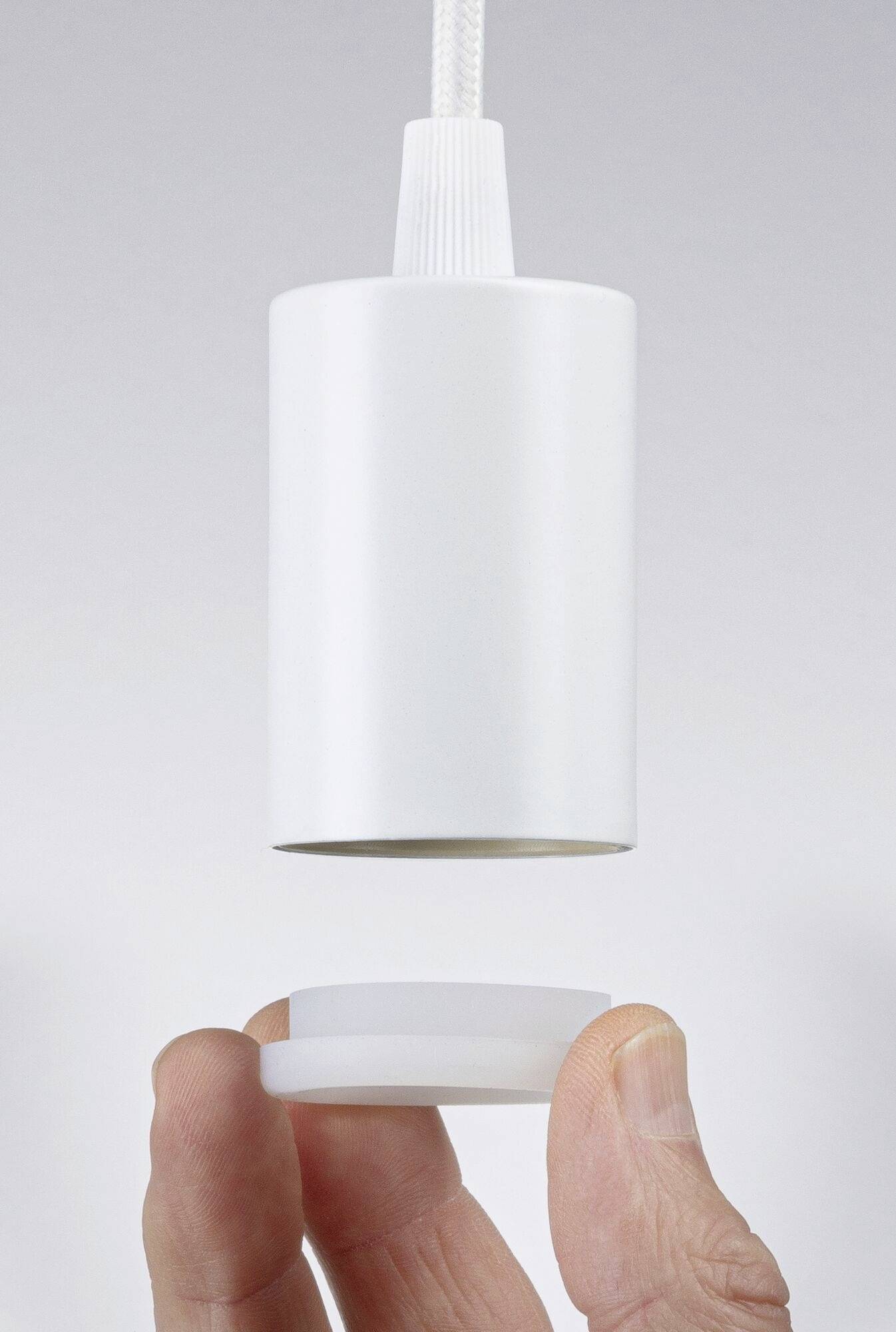 Des mains tiennent un couvercle blanc cylindrique sous un dispositif approprié. La scène montre un montage ou une installation potentielle.