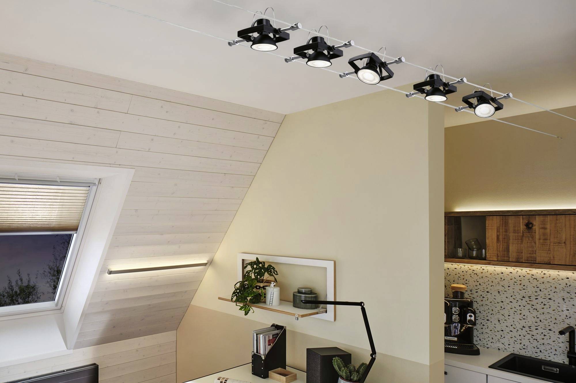 Une cuisine moderne avec un plafond en bois incliné. Cinq spots au plafond éclairent la pièce. Des plantes et de la décoration sont disposées sur l'étagère murale.