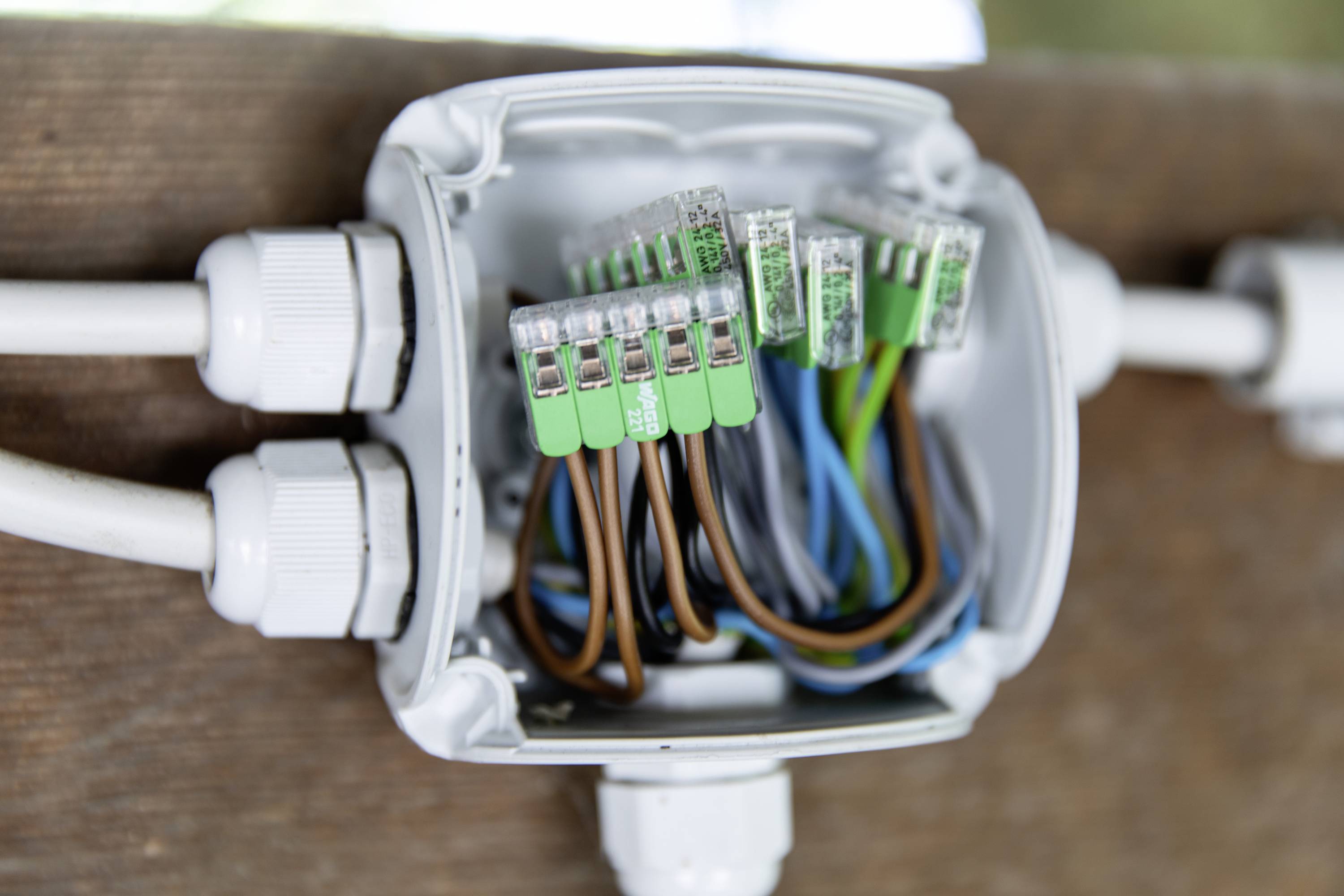 Une boîte de dérivation ouverte avec différents câbles de couleurs fixés par des bornes montre une connexion électrique.