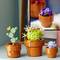 Trois ensembles de cactus LEGO dans des pots de fleurs : un cactus vert avec une fleur jaune, un cactus avec des épines jaunes et des fleurs mauves, et un petit cactus au bord orangé et aux fleurs roses.