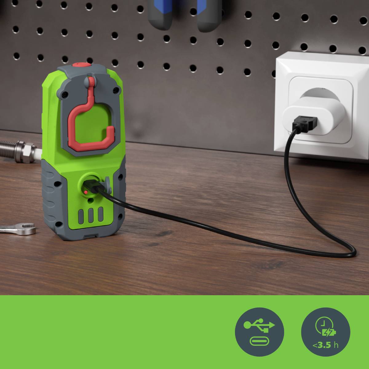 Un chargeur vert est branché à une prise électrique. Une clé à molette est posée au premier plan. Des outils sont suspendus en arrière-plan.