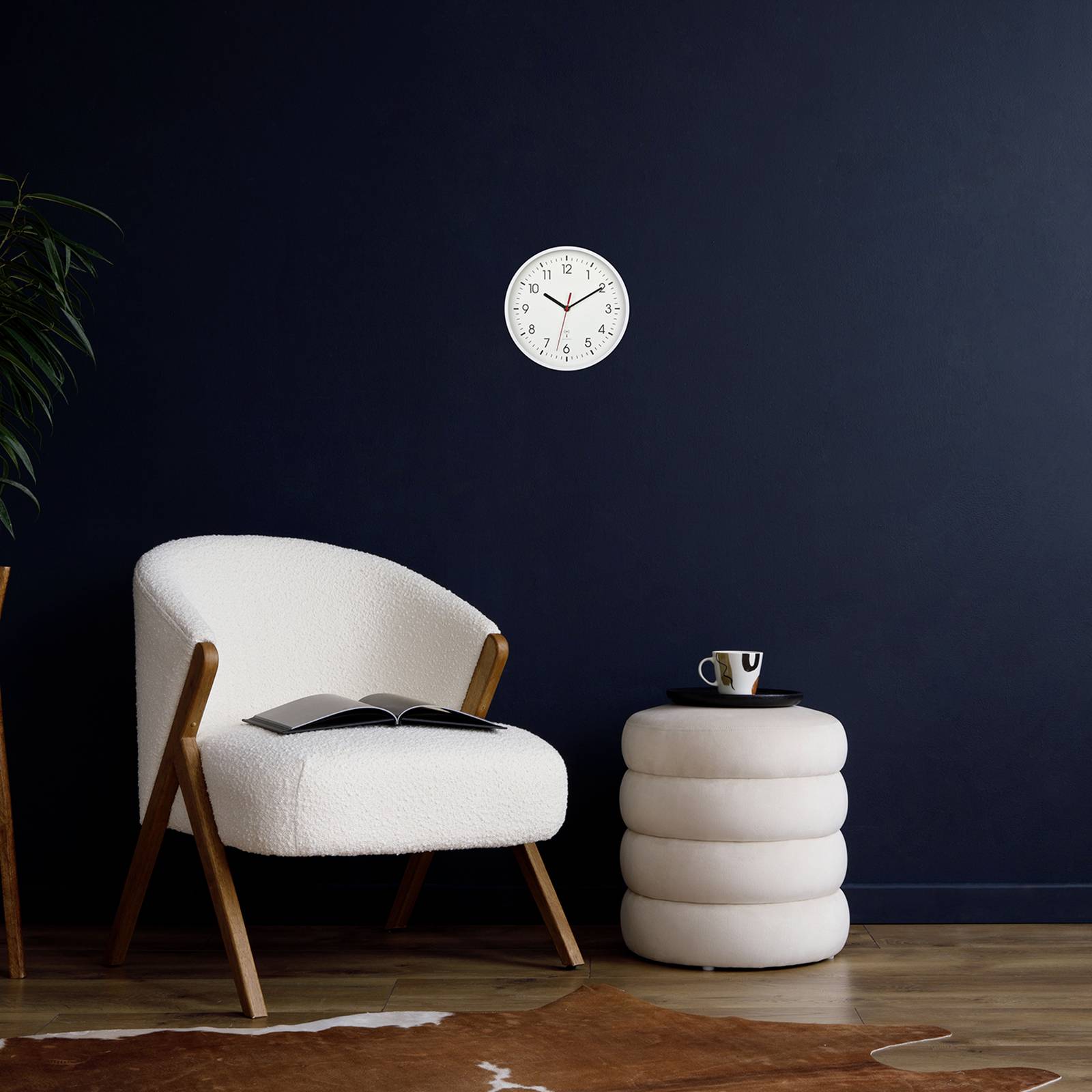 Un fauteuil beige et un tabouret d'appoint avec une tasse devant un mur bleu marine. Une horloge indique 10:09.