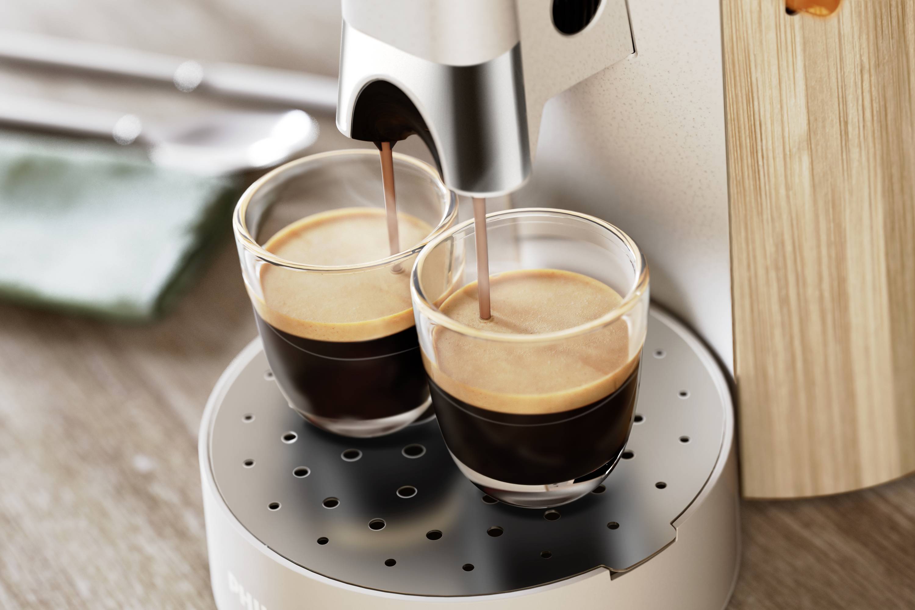Deux espressos sont versés simultanément dans des verres depuis une machine à café. La machine est posée sur une surface en bois.