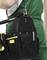 Une personne en tenue de travail verte tient un sac à outils noir avec une poignée jaune, contenant divers outils et un stylo à bille.