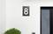 Une façade blanche avec une porte d'entrée et le numéro de maison '8'. Un petit buisson se trouve à gauche de la porte.