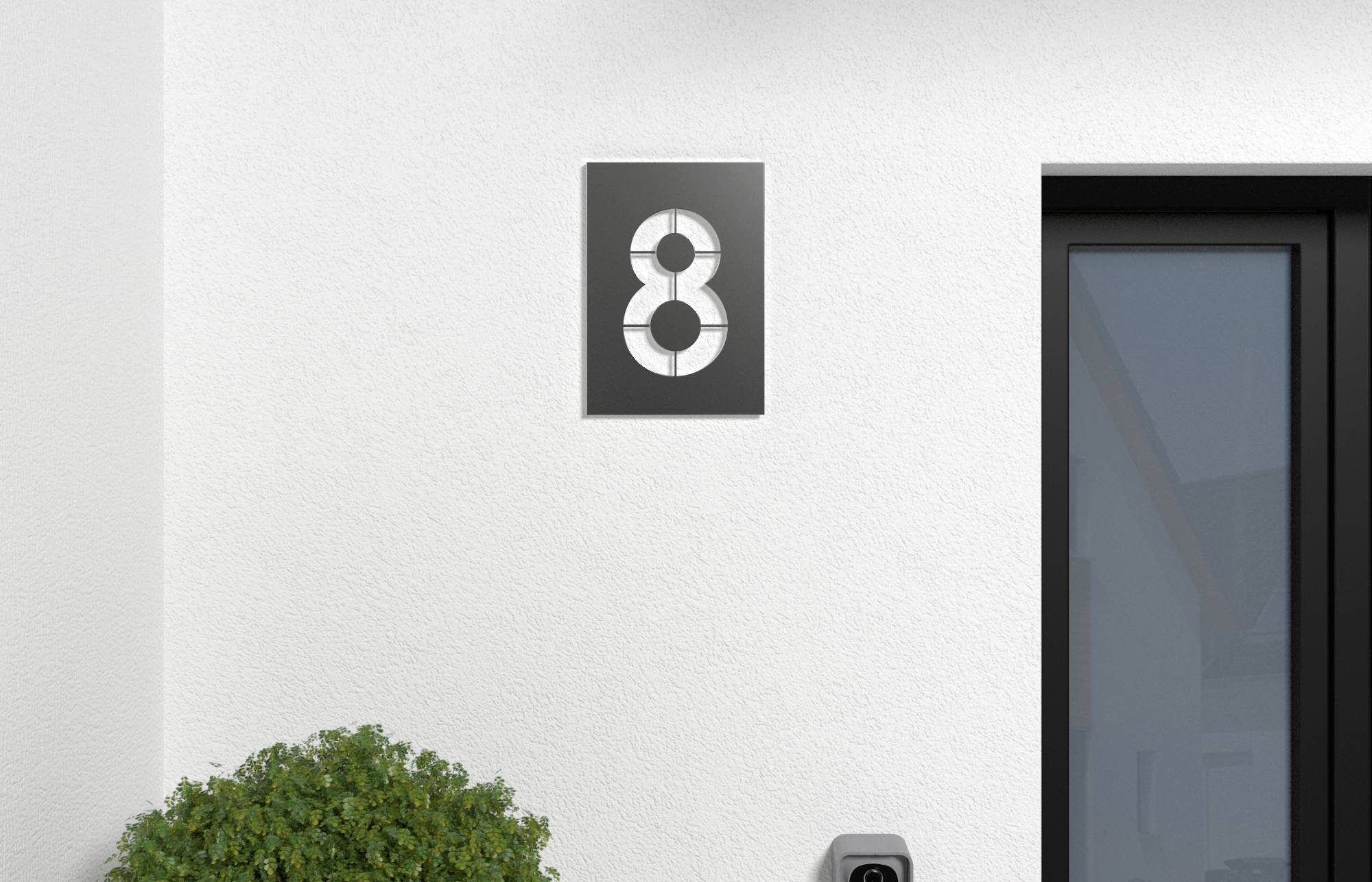 Extérieur d'une maison moderne avec une plaque numéro 8 noir montée sur un mur blanc à côté d'une porte à cadre foncé et un arbuste.