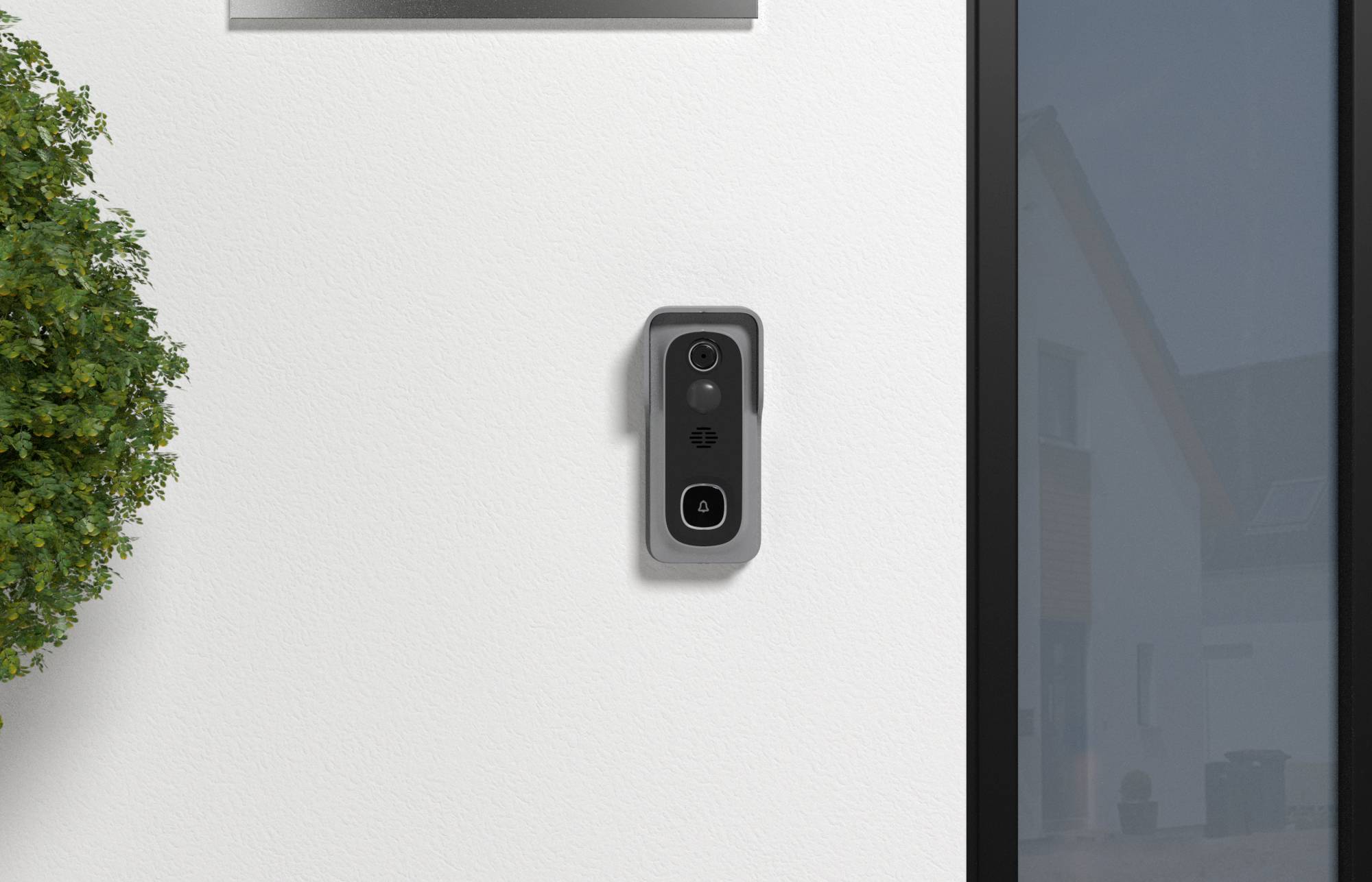 Une sonnette vidéo noire montée sur un mur extérieur blanc à côté d'une porte vitrée, avec une plante partiellement visible sur la gauche.