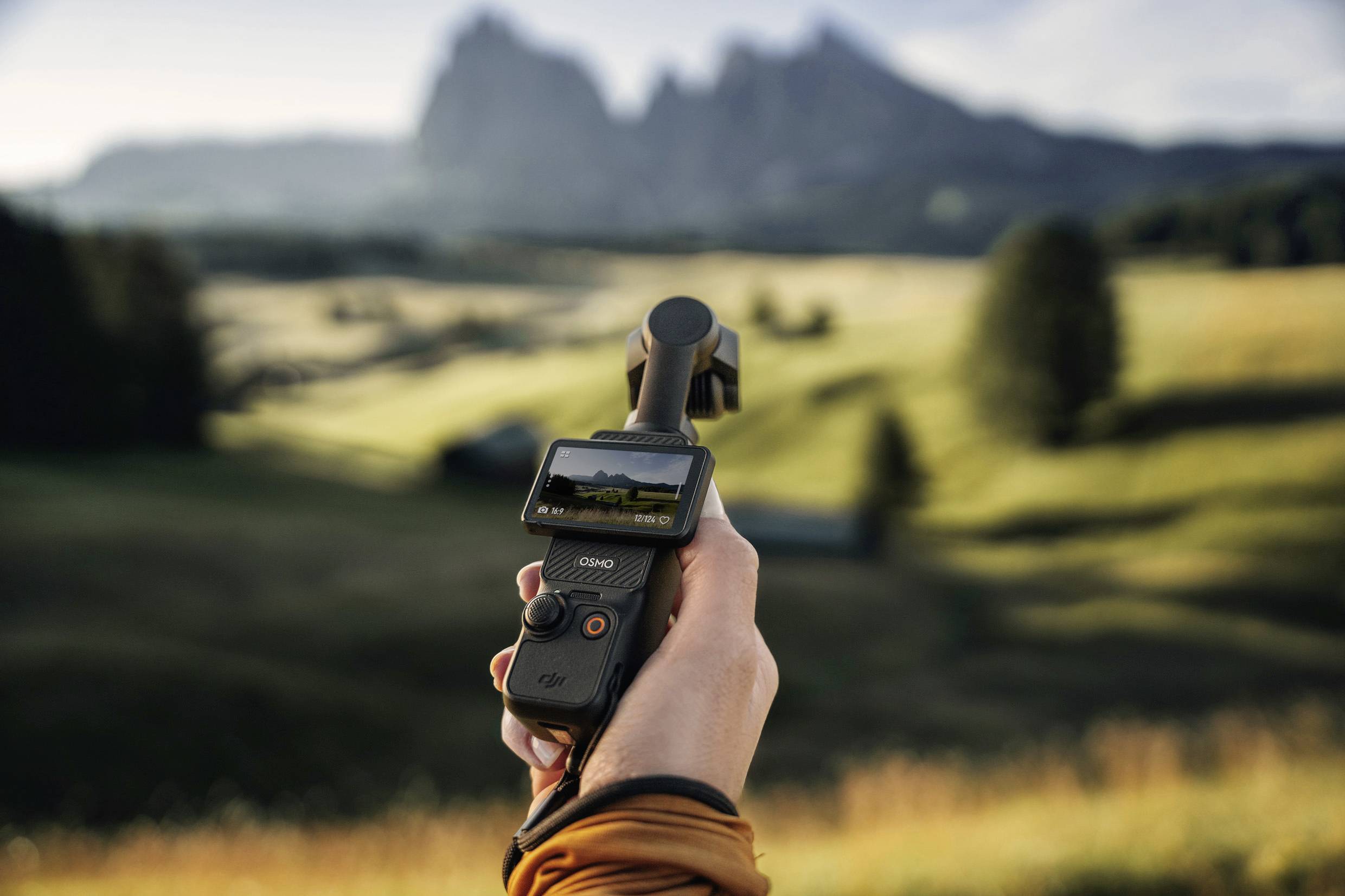 Une personne tient une caméra à la main et filme un paysage avec des montagnes en arrière-plan.