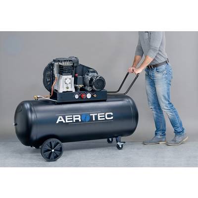 Une personne pousse un grand compresseur d'air noir sur roulettes. Sur le compresseur est inscrit 'AEROTEC'.