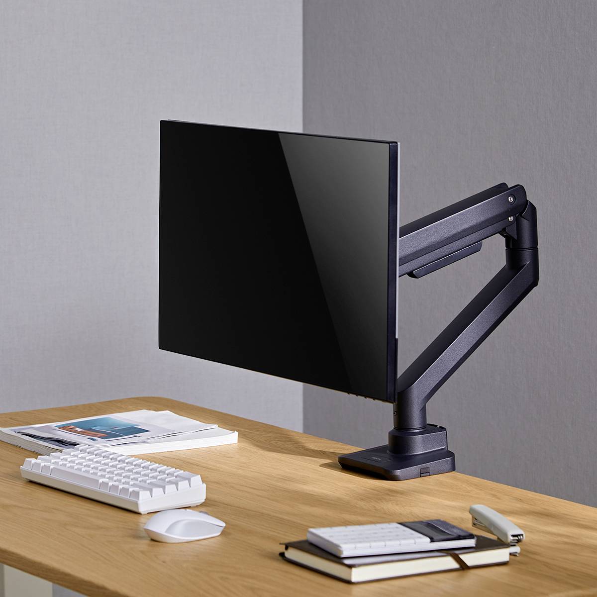 Un bureau propre avec un moniteur d'ordinateur sur un bras articulé, un clavier et deux livres ; environnement moderne et minimaliste.
