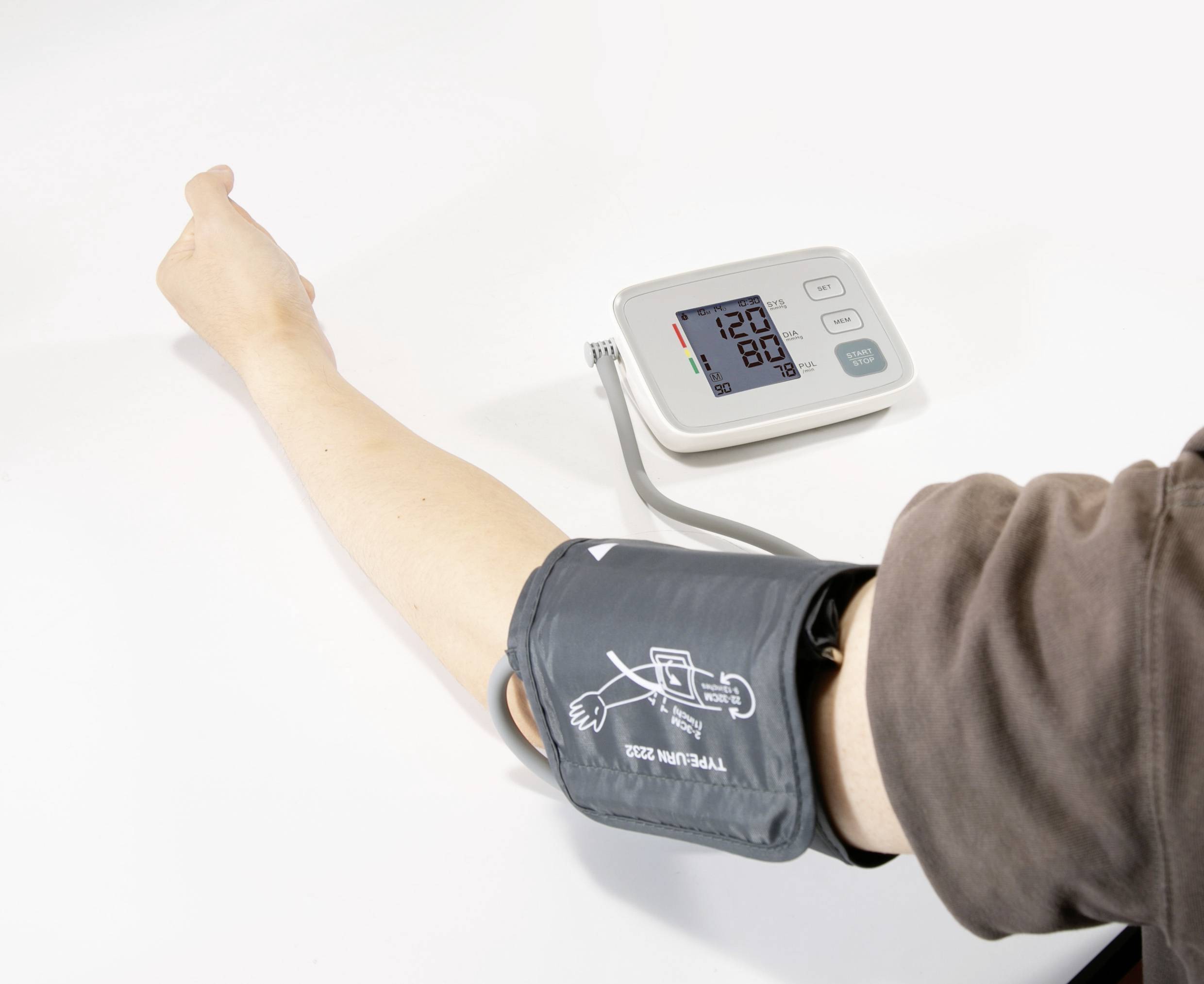 Une personne mesure sa tension artérielle à l'aide d'un appareil numérique. L'écran affiche 120 sur 80. Un bras est allongé sur une table.