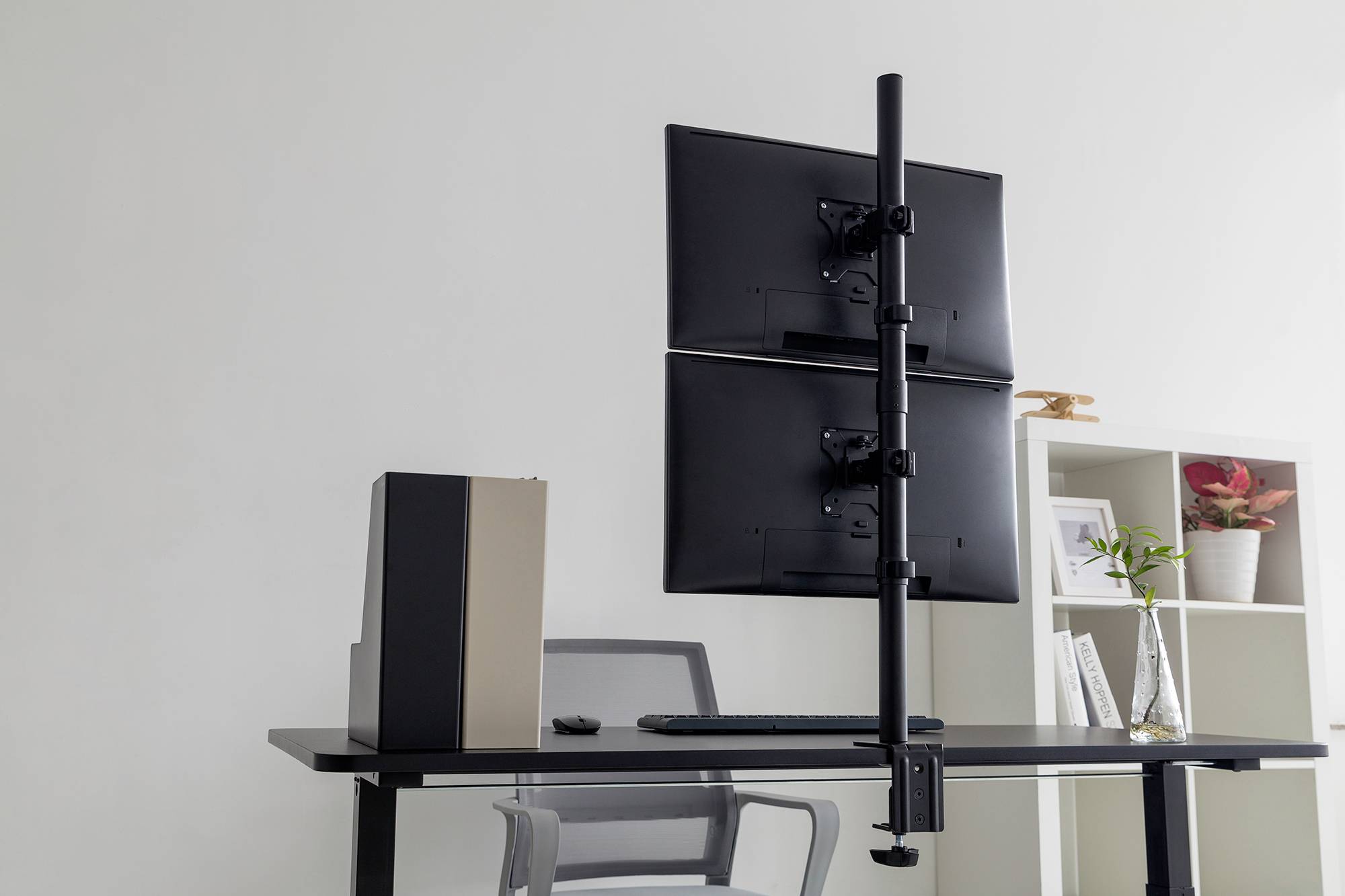 Bureau moderne avec deux écrans montés verticalement, un clavier, un classeur créatif et une étagère avec des plantes en arrière-plan.