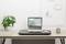 Un bureau bien rangé avec un ordinateur portable, une souris, un pot de plante et des fournitures de bureau, devant un mur grillagé blanc avec des cartes.