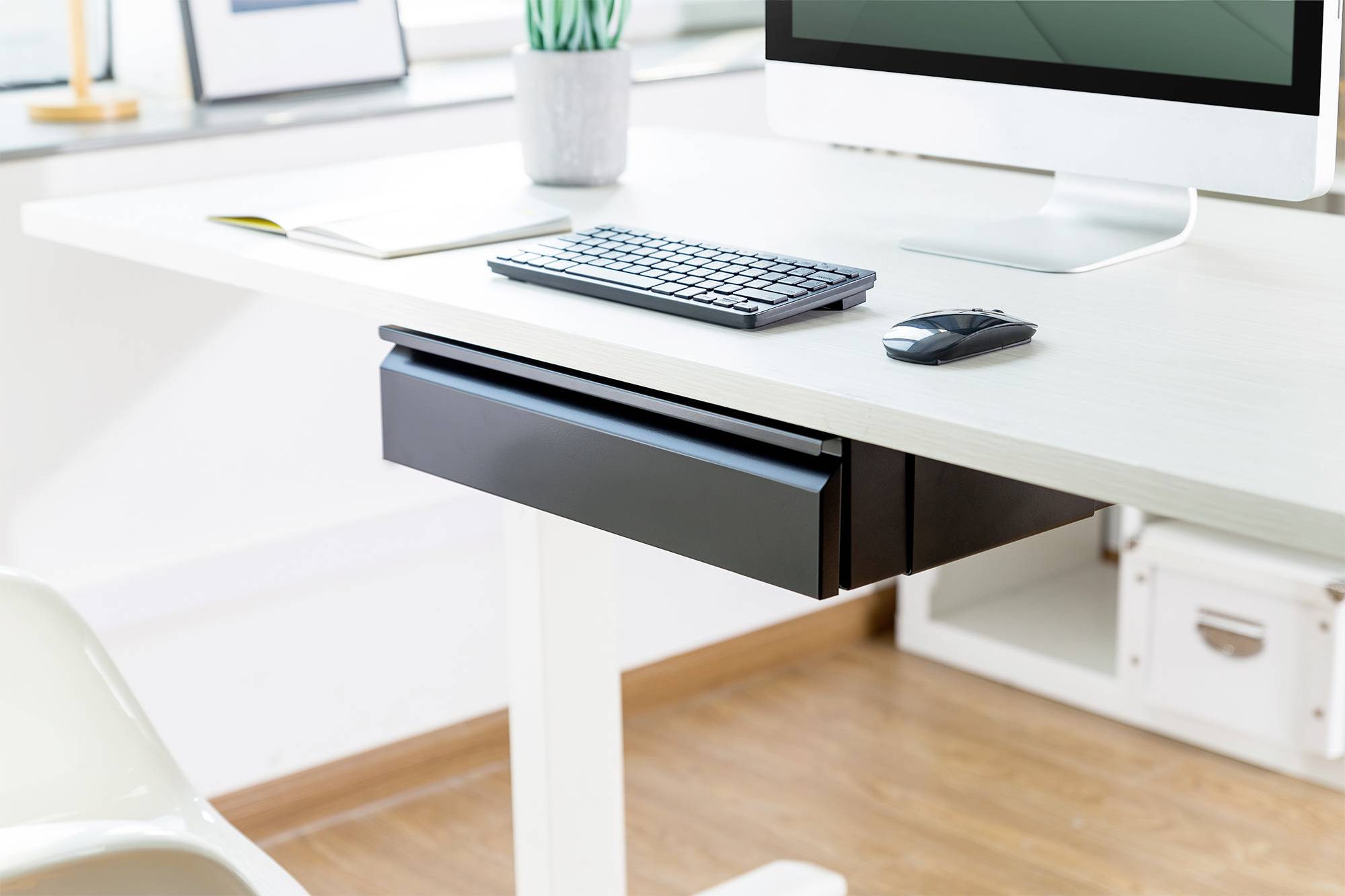 Espace de travail moderne et lumineux avec un ordinateur, un clavier et une souris sur un bureau blanc. Des plantes et des fournitures de bureau sont visibles en arrière-plan.
