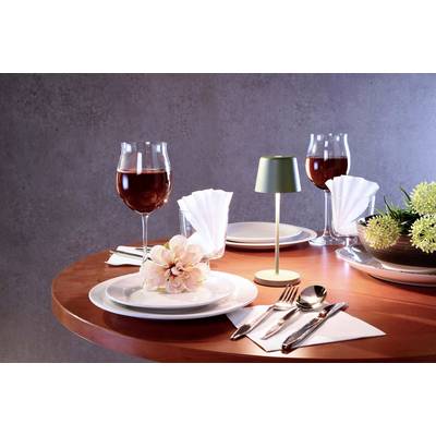 Une table ronde est élégamment dressée avec des verres à vin, des couverts, des serviettes et des fleurs. Deux verres de vin rouge sont prêts.