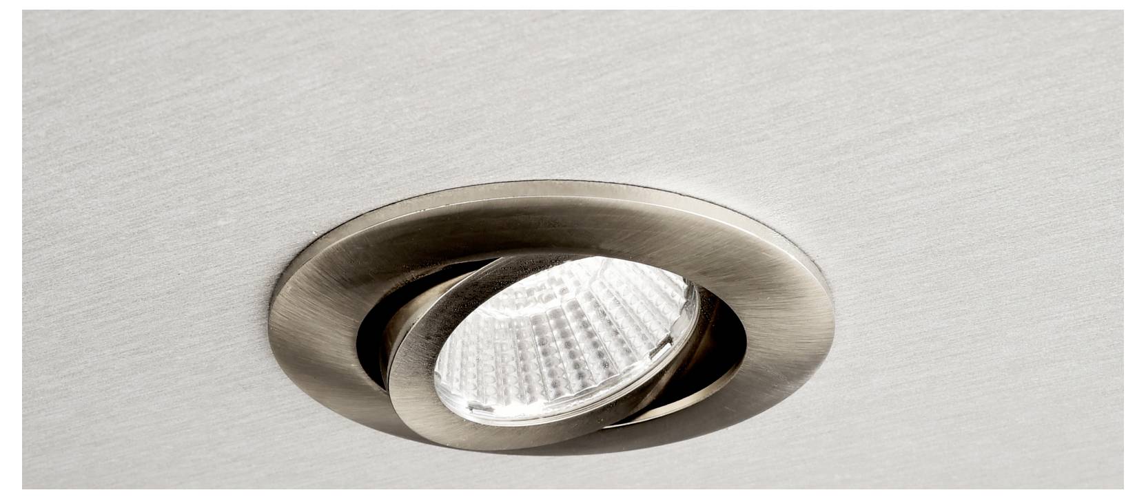 Gros plan sur un spot LED encastré et rond, à collerette en métal brossé, installé dans un plafond.