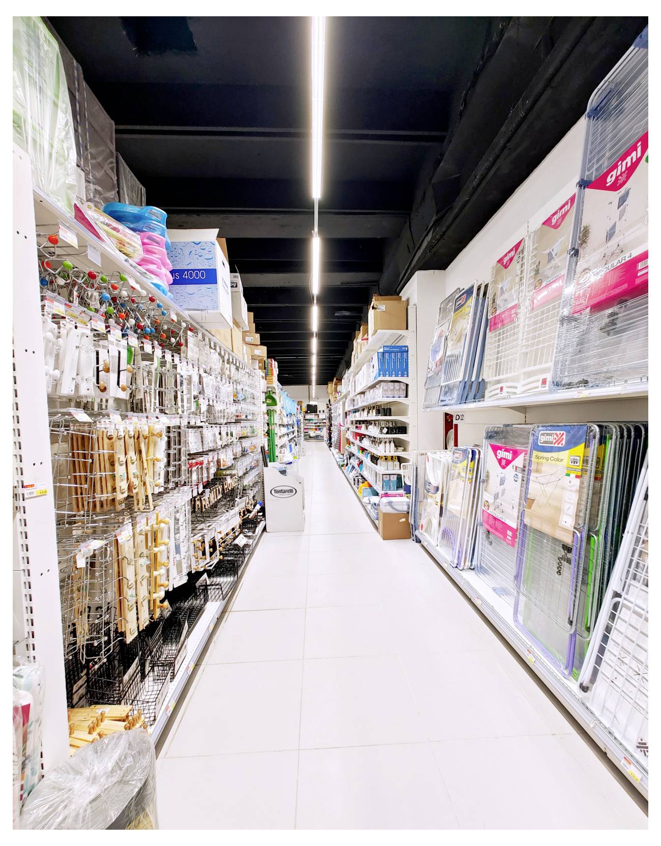 Une longue allée dans un magasin d'articles pour la maison, avec des étagères de paniers, de rangements et d'organiseurs des deux côtés, sous des plafonniers lumineux.