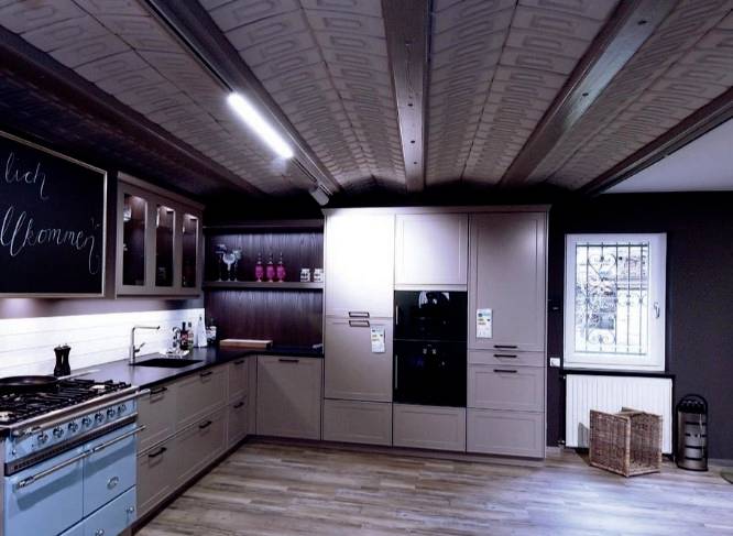 Cuisine moderne avec des appareils encastrés, un plan de cuisson bleu et un sol en bois. Un tableau est accroché au mur avec l'inscription 'Bienvenue'.