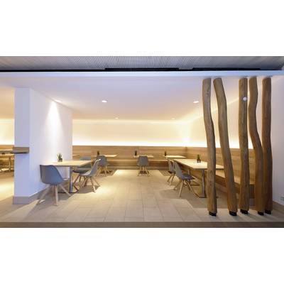 Espace de restauration moderne avec des tables en bois clair et des chaises grises, un éclairage discret, des éléments décoratifs en bois séparant l'espace.