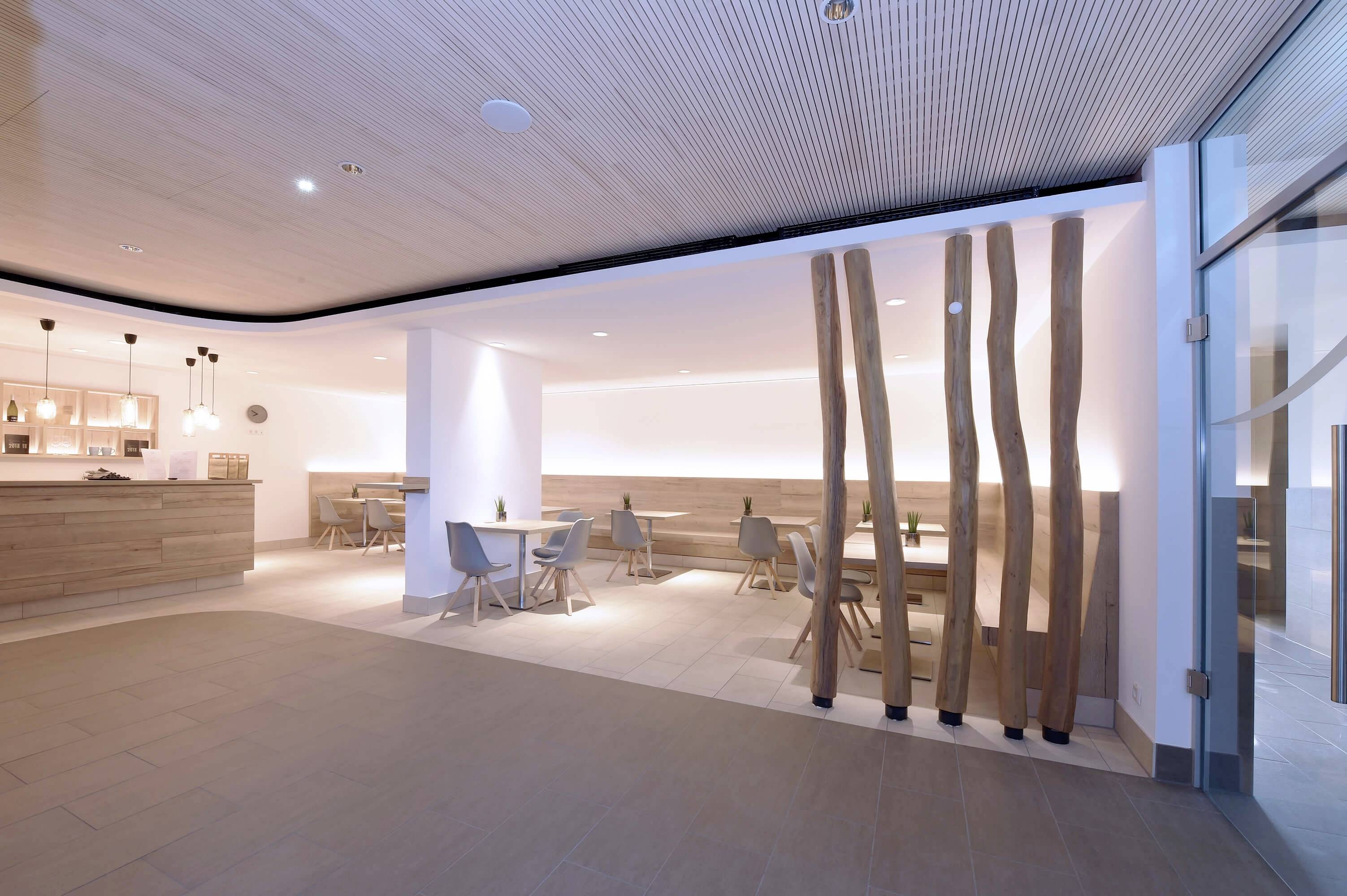 Intérieur moderne et lumineux d'un restaurant avec des tables et des chaises en bois. Des éléments en bois aux formes ondulantes divisent l'espace. Éclairage discret.