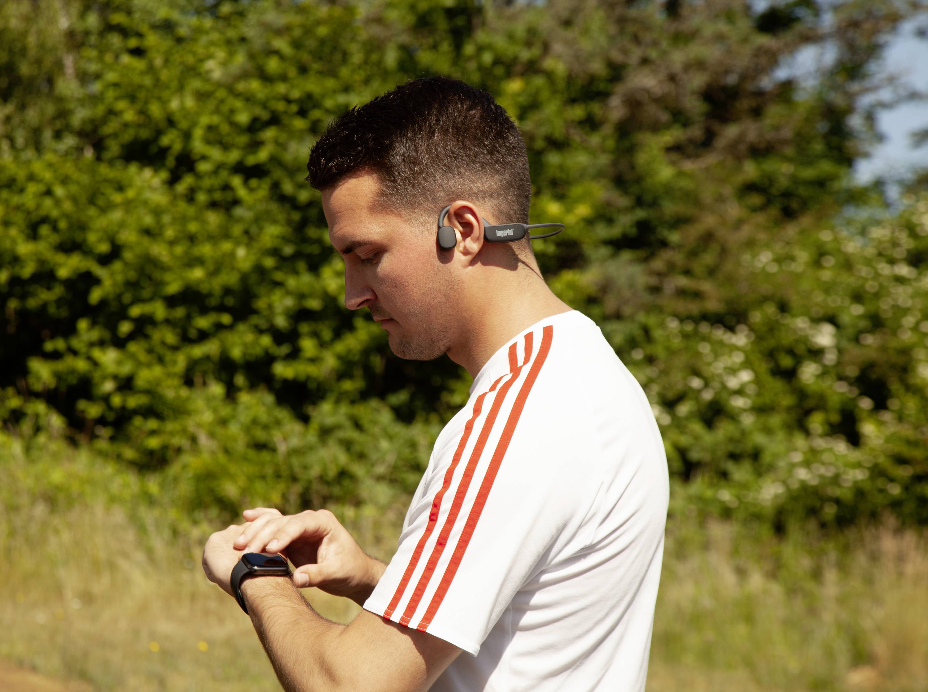 Une personne en tenue de sport vérifie un appareil sur son poignet, probablement une montre connectée, alors qu'elle se trouve à l'extérieur.