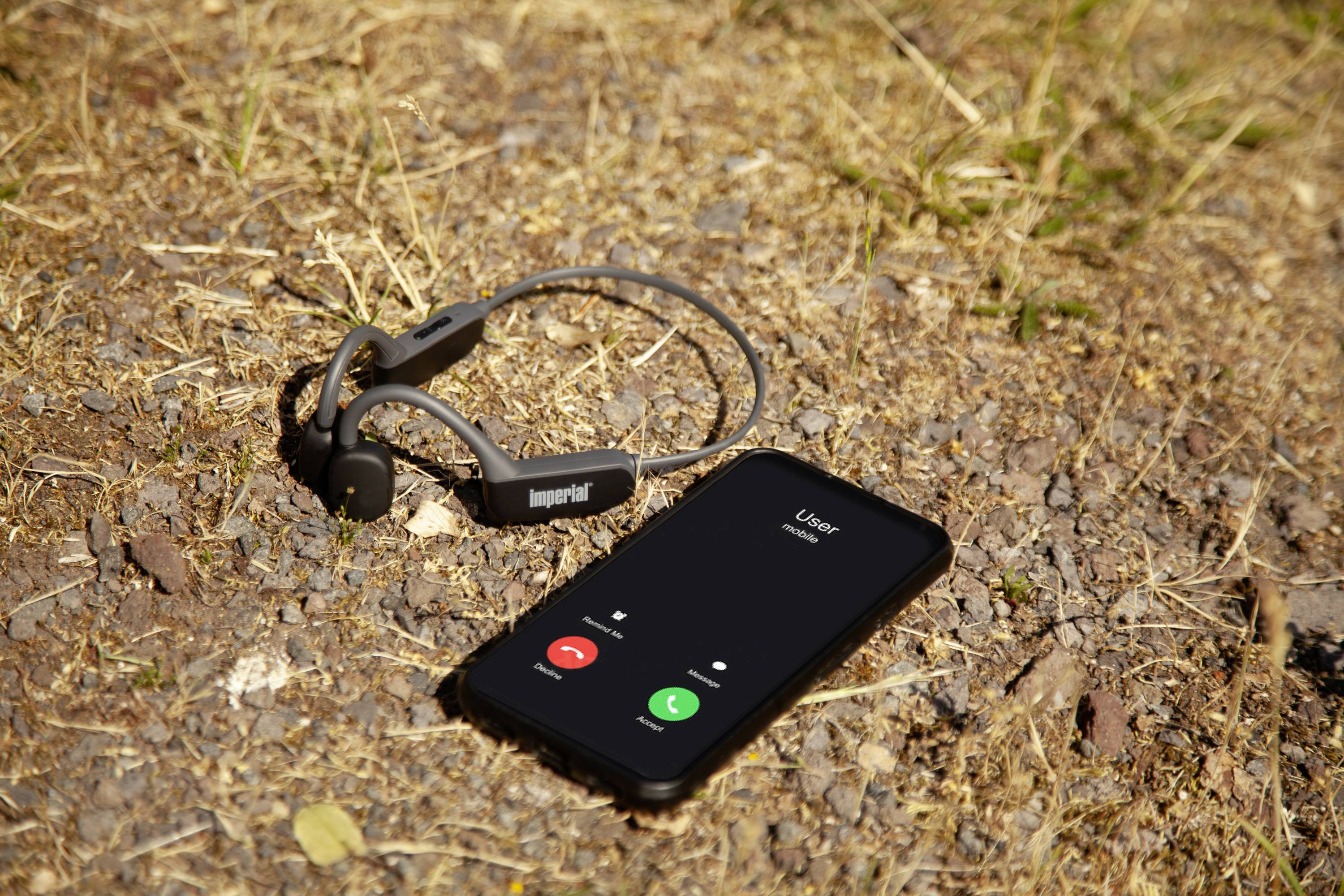 Un smartphone sur de l'herbe sèche affiche un écran d'appel entrant, à côté duquel se trouve un casque sans fil.