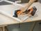 Une personne ponce le bord d'un cadre en bois avec un outil électrique oscillant sur une table.