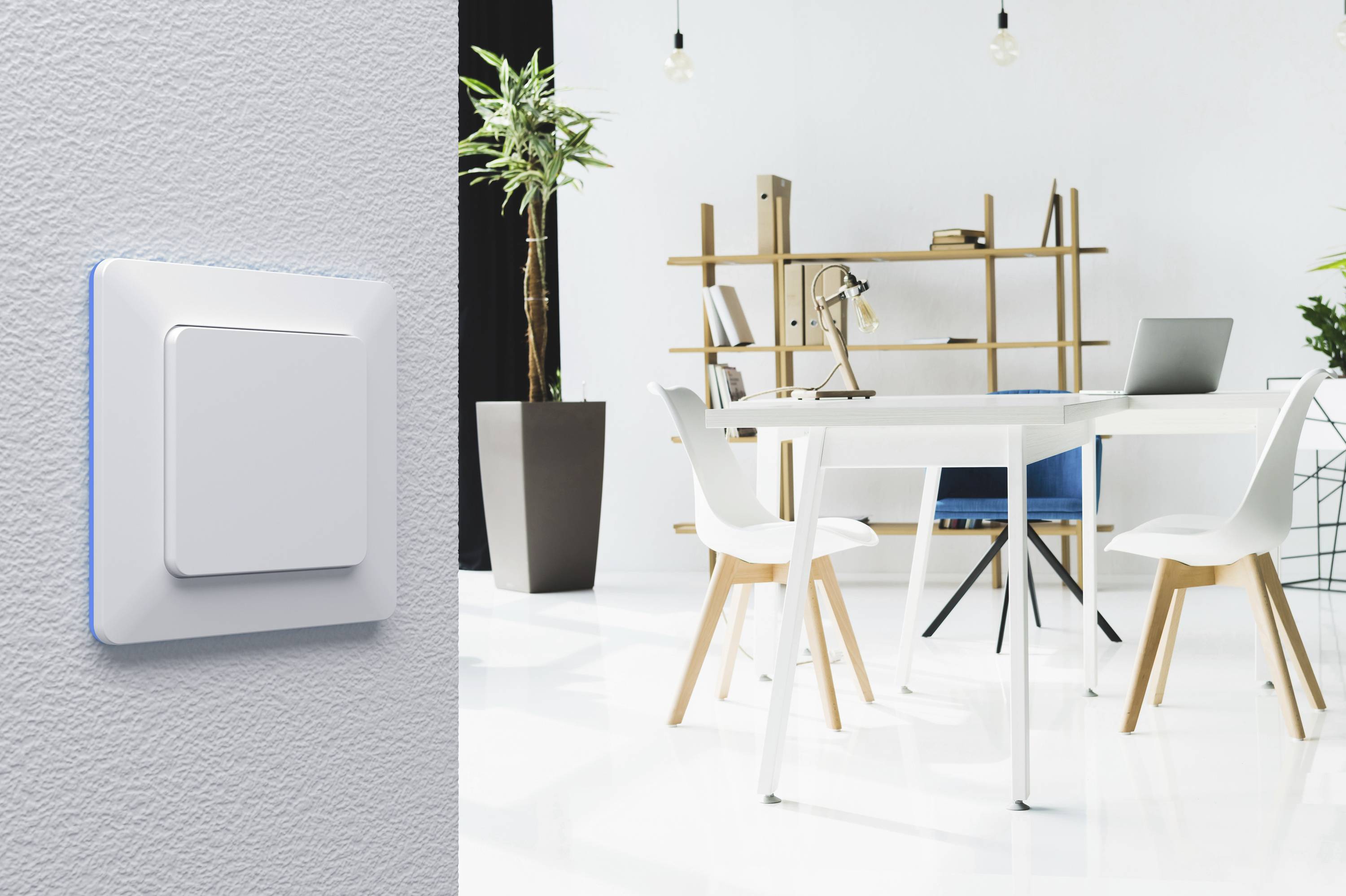 Interrupteur sur un mur gris, espace de bureau moderne et lumineux en arrière-plan avec une table, des chaises, un ordinateur portable et des plantes.