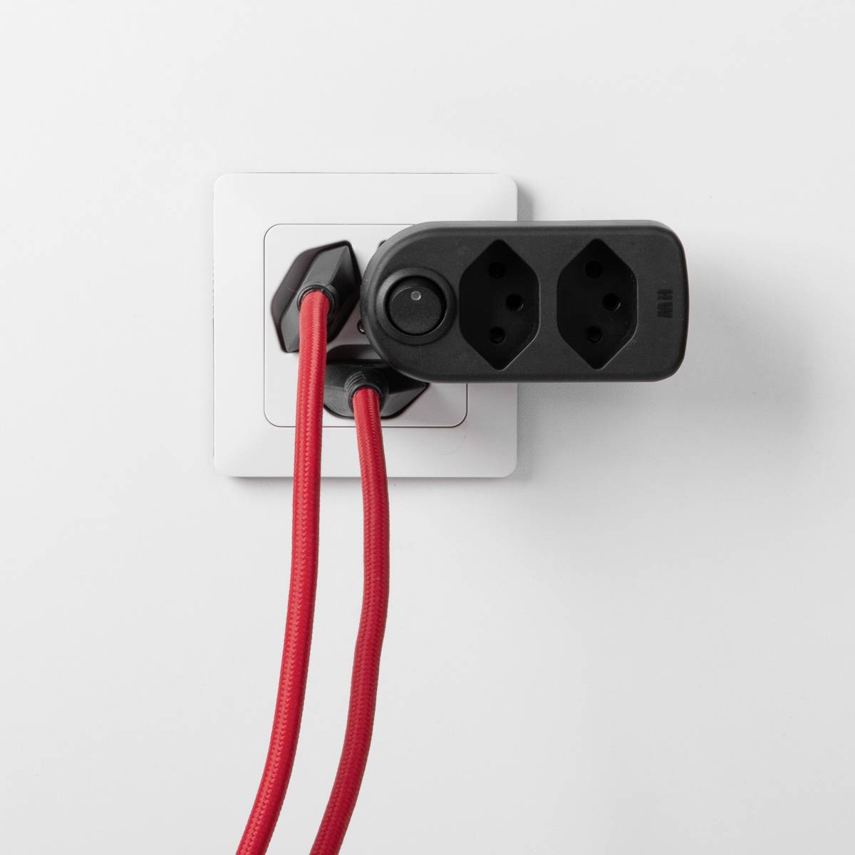 Une prise murale avec une rallonge électrique et deux câbles rouges partant d'un adaptateur double.