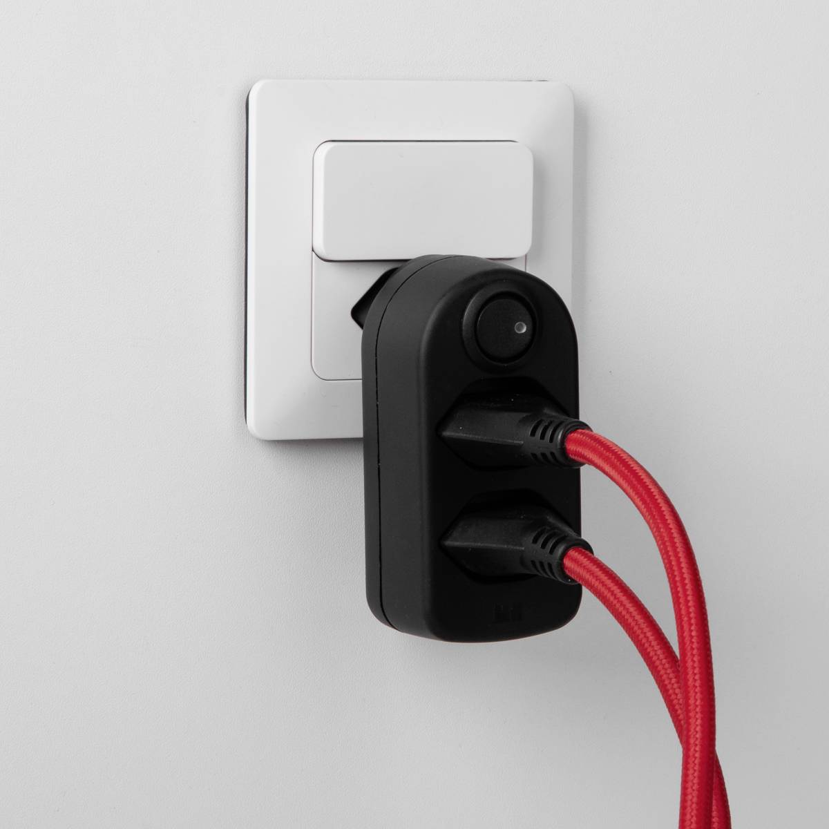 Deux fiches noires dans une prise noire avec un câble rouge, branchées à une prise murale blanche.
