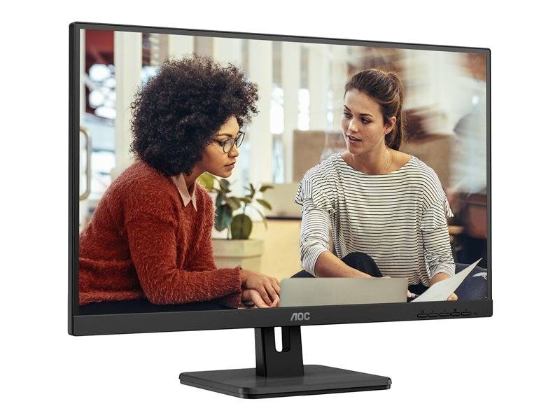 Deux personnes discutent à une table, regardant un ordinateur portable. Des meubles de bureau flous sont visibles en arrière-plan.